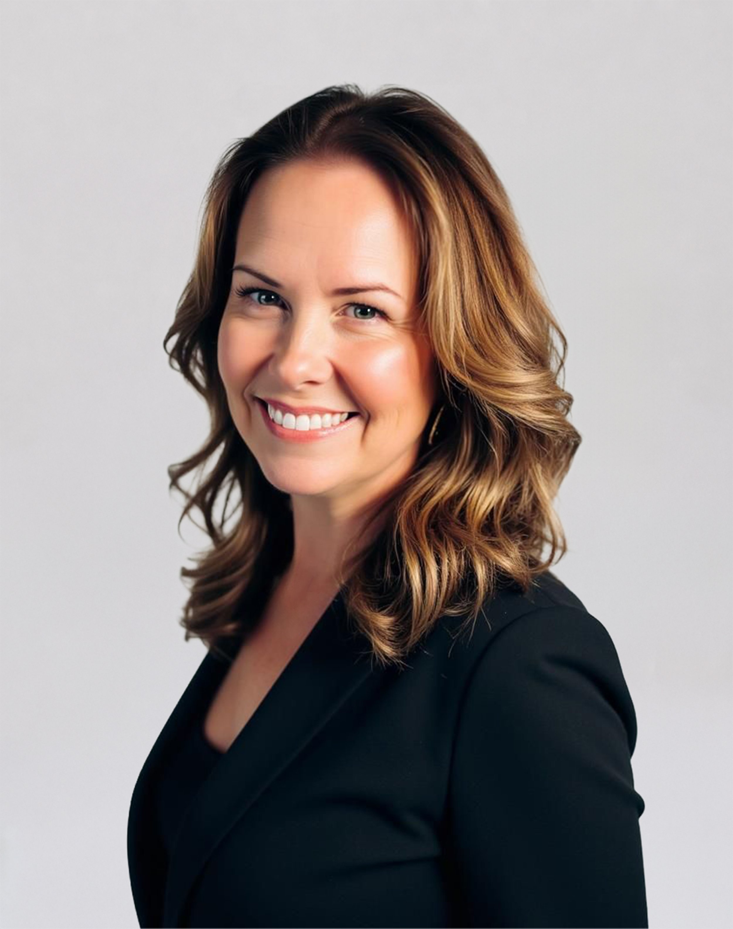 Professional headshot of a smiling woman with shoulder-length brown hair, wearing a black blazer against a light gray background.