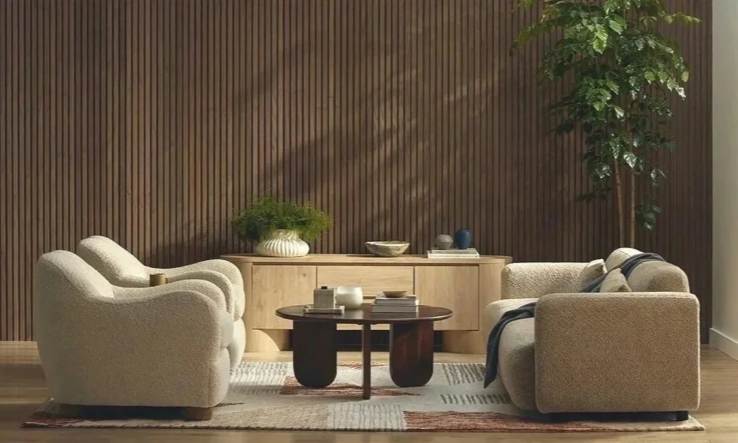 Warm, modern living room with curved neutral sofas, a dark round coffee table, light wood cabinetry, and vertical wood-paneled walls.