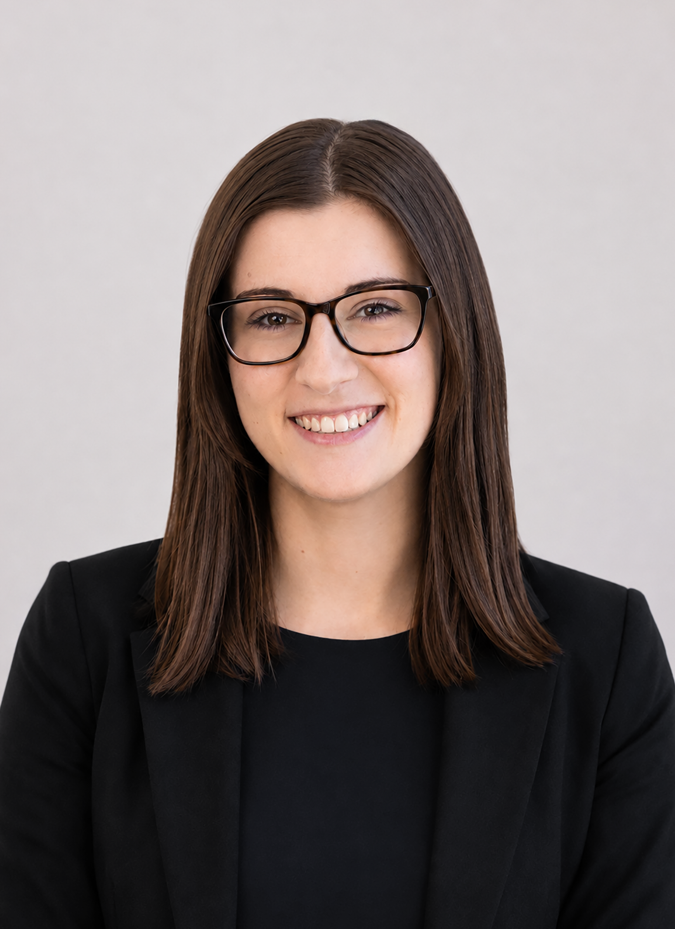 Professional headshot of a smiling woman with straight dark brown hair and black glasses, wearing a black blazer against a light gray background.