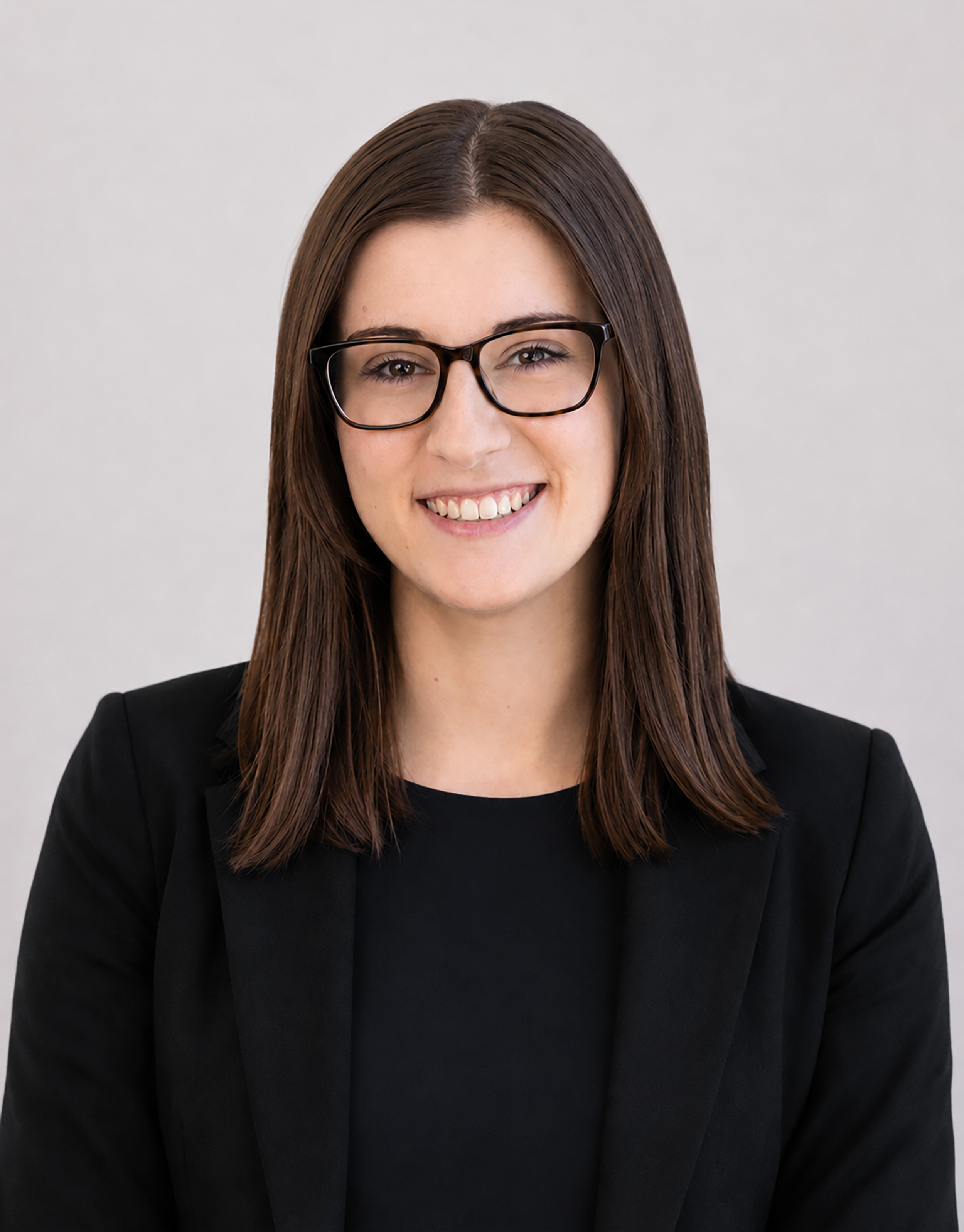Professional headshot of a smiling woman with straight dark brown hair and black glasses, wearing a black blazer against a light gray background.