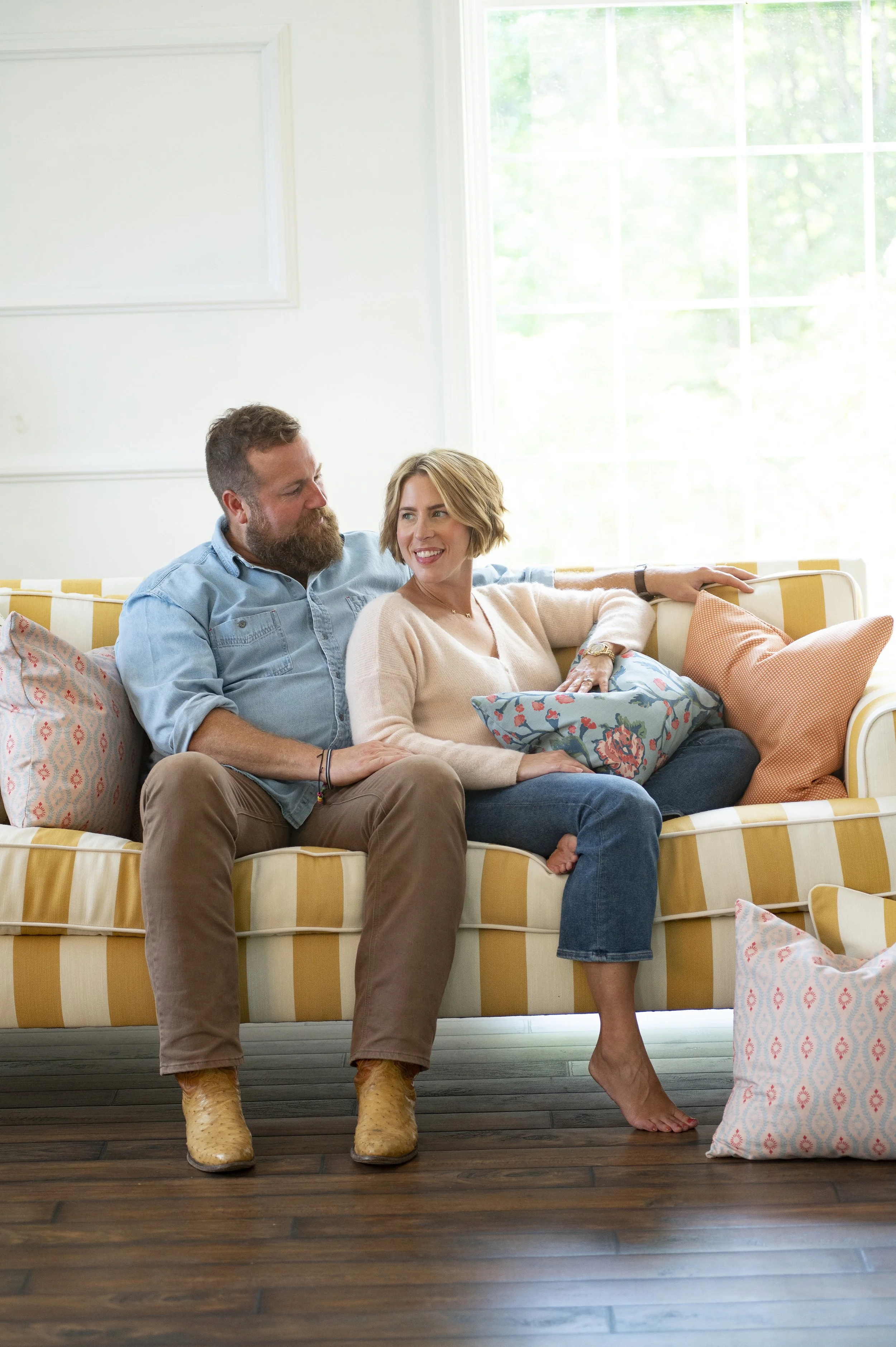 Relaxed couple sitting closely on a yellow-and-white striped sofa surrounded by colorful patterned pillows.