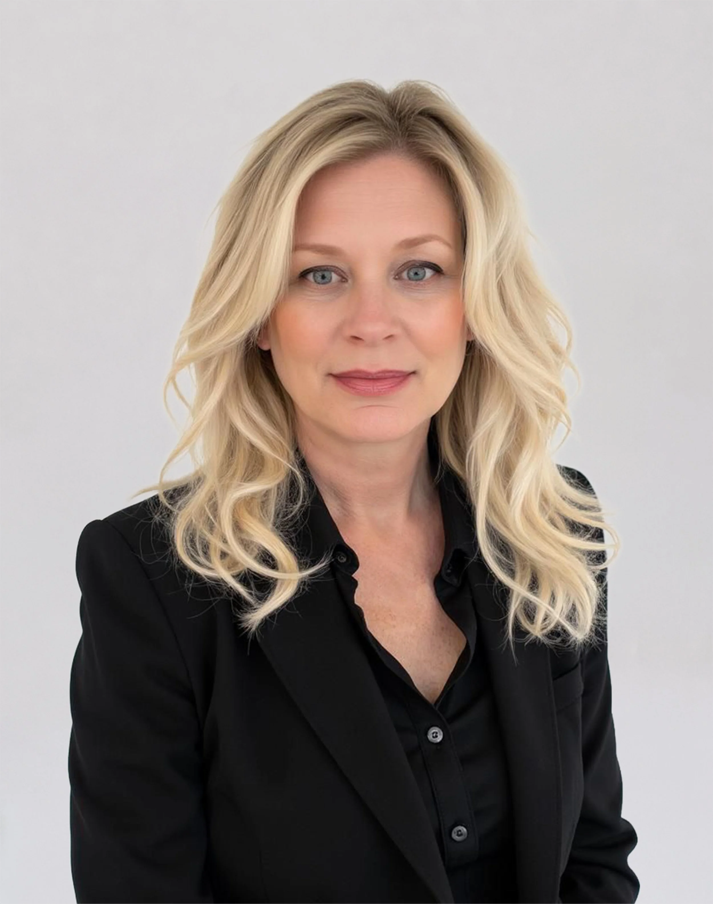 Professional headshot of a woman with long blonde hair, wearing a black blazer and black blouse against a light gray background.