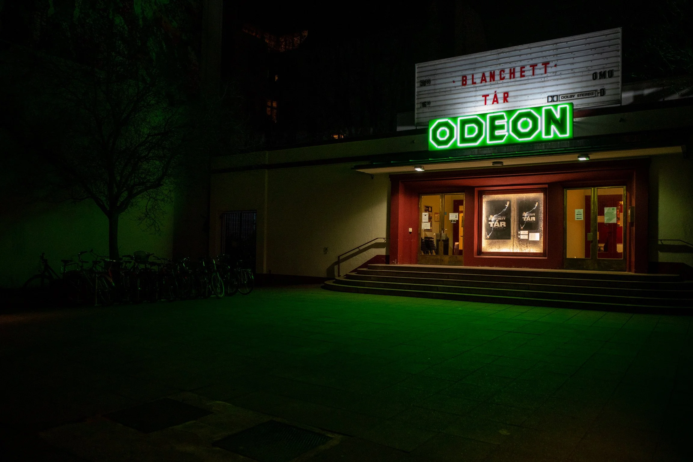Außenansicht eines Kinos mit dem leuchtenden Schild "ODEON" und Plakatwerbung für den Film "Tár". Vor dem Kino sind Fahrräder abgestellt.