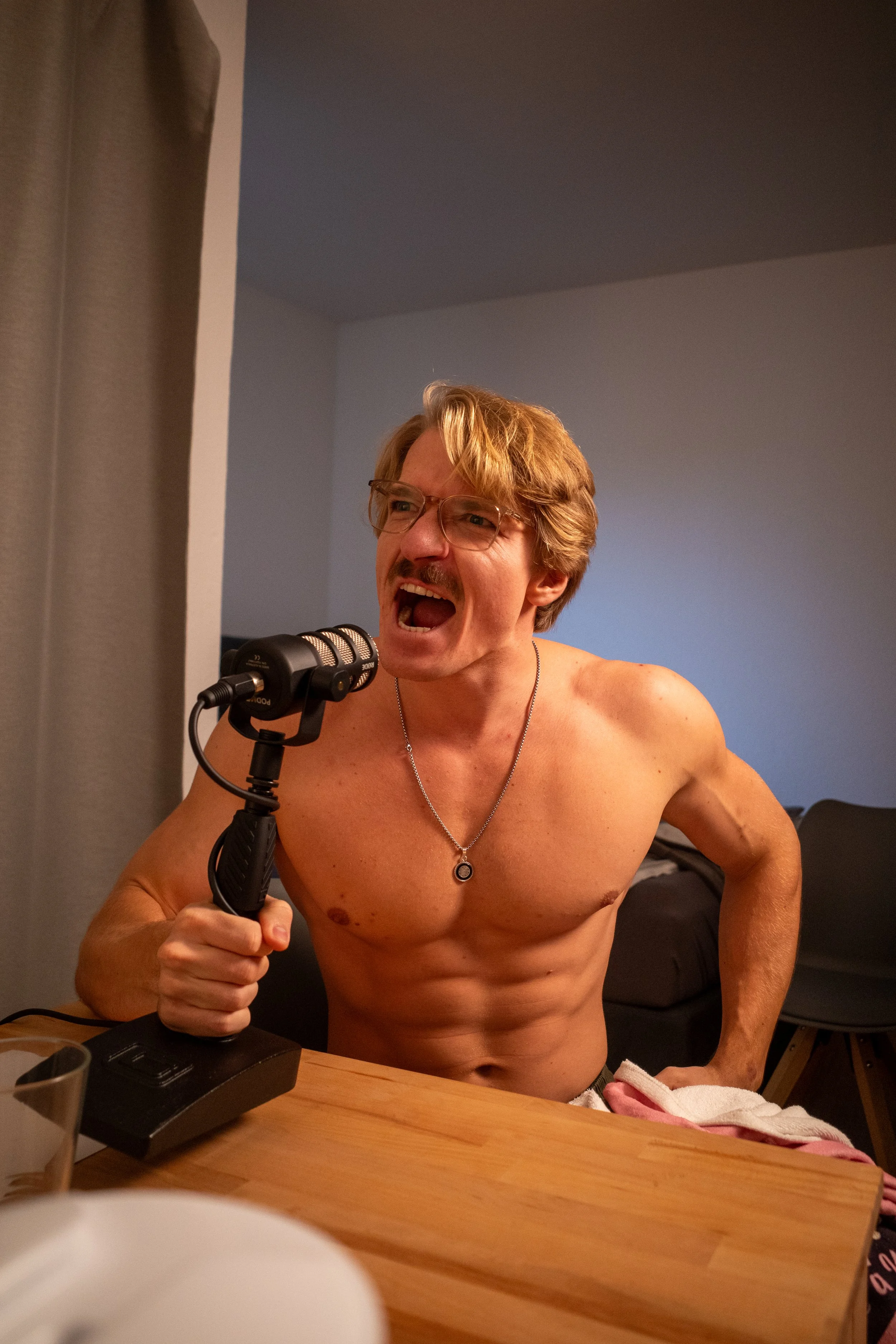 Ein Mann ohne Hemd sitzt an einem Tisch und spricht in ein Mikrofon.
