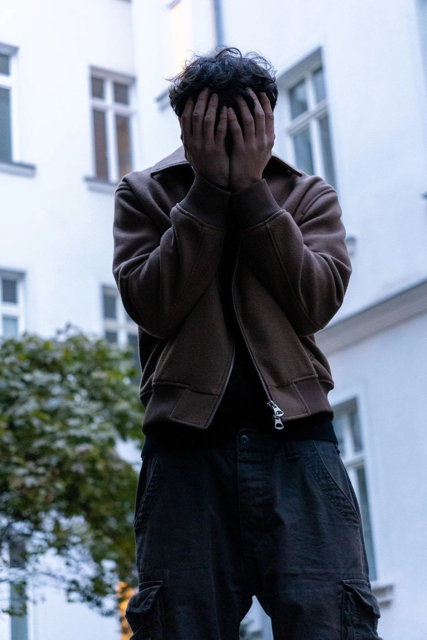 Mann hält sein Gesicht mit den Händen verdeckt vor einem Gebäude.