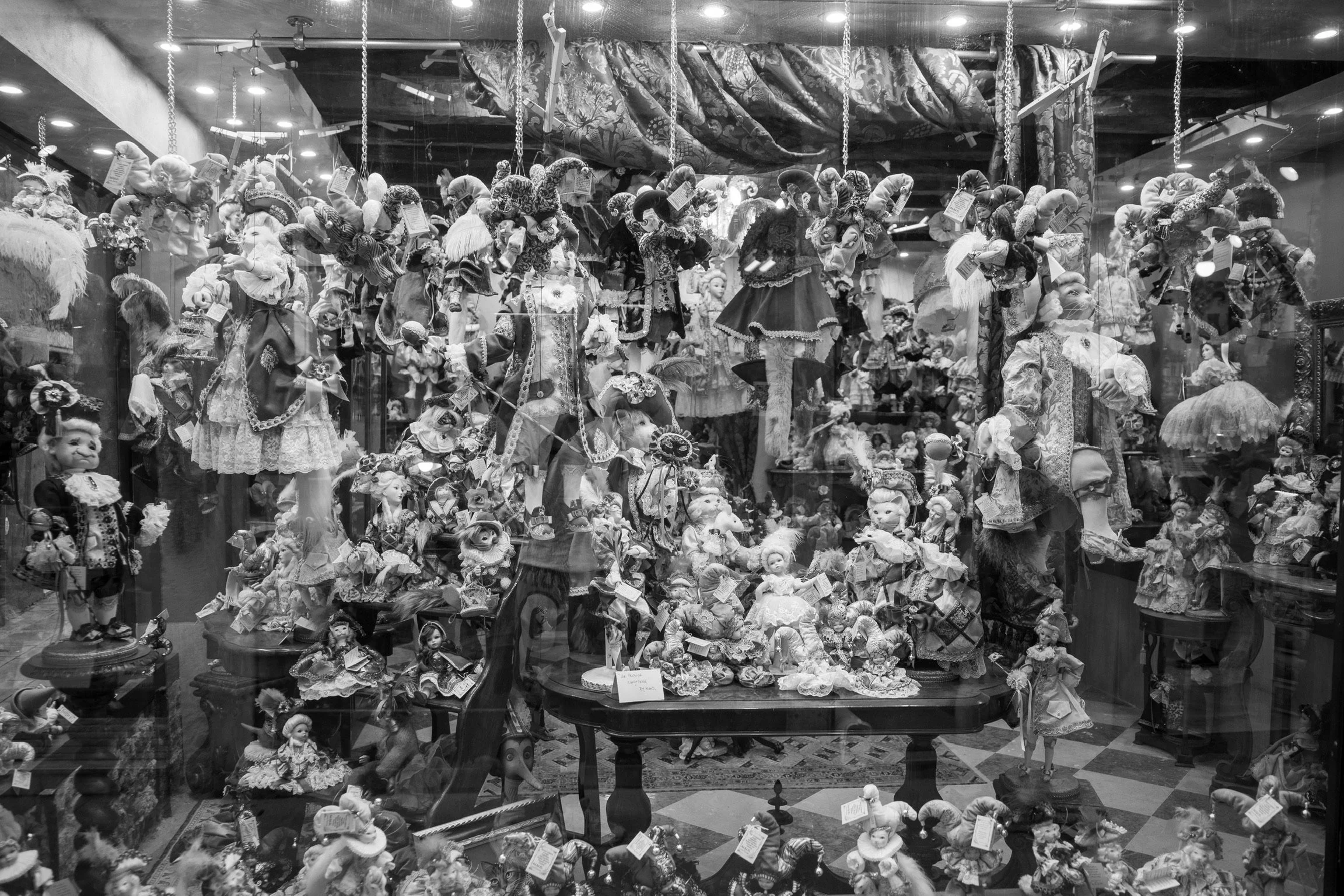Schaufenster mit einer Vielzahl an Puppen und Masken in aufwendigen Kostümen in einem Geschäft, beleuchtet von Deckenstrahlern.