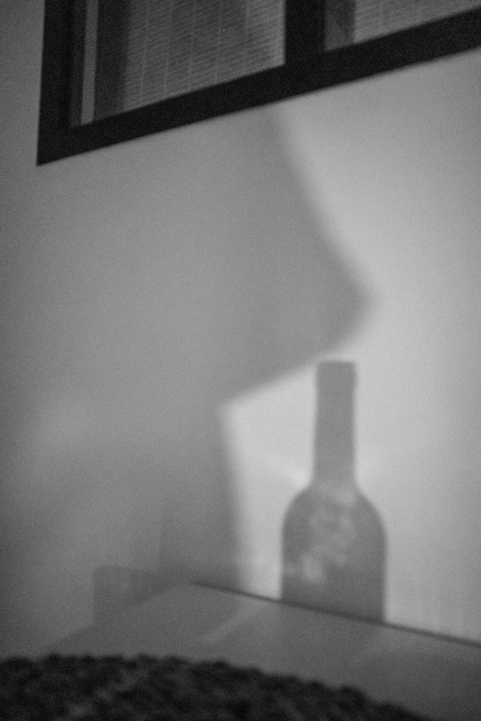 Schwarzweißfoto einer Schattenprojektion einer Flasche auf einer Wand.