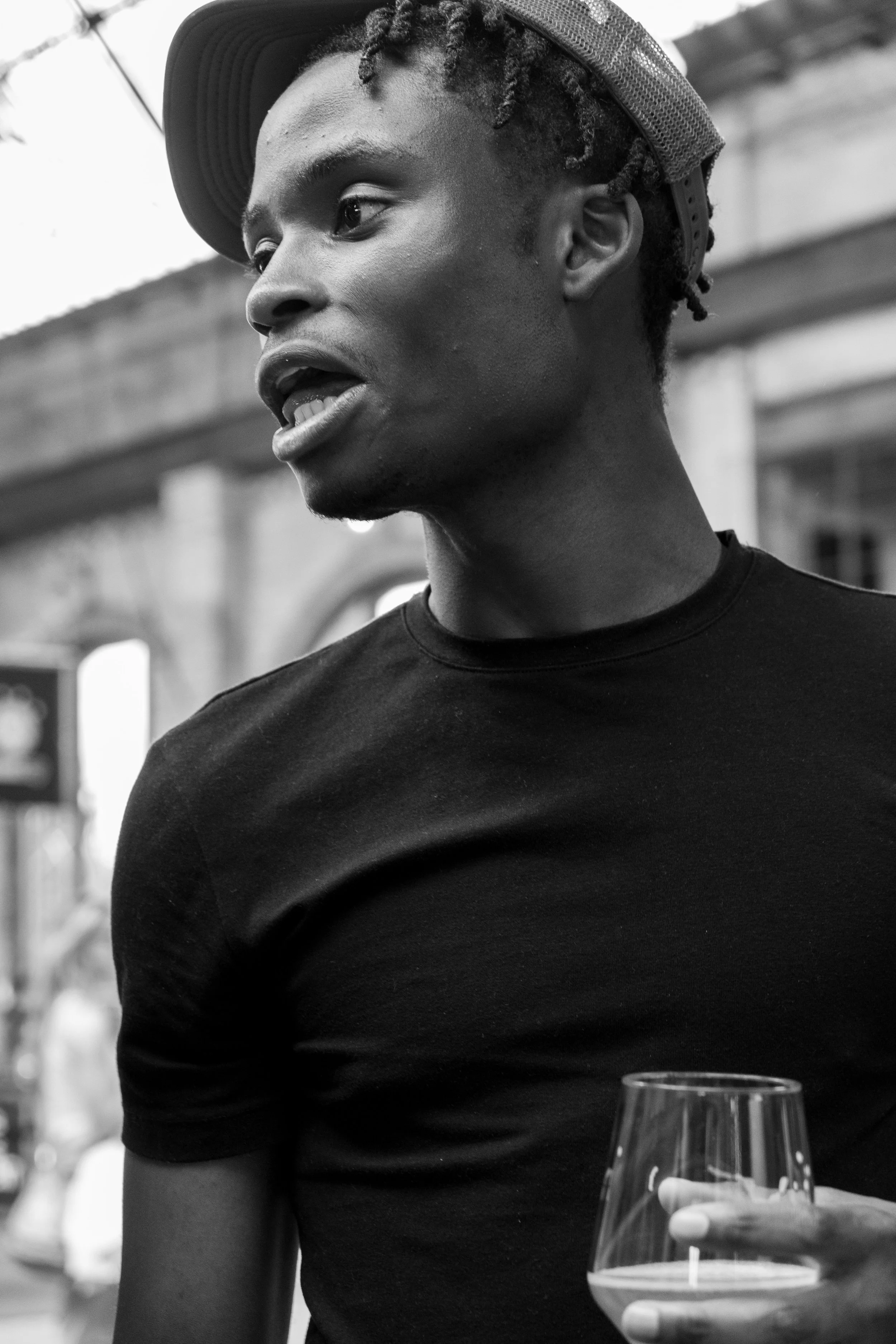 Schwarz-weiß-Foto eines Mannes mit Baseballkappe und T-Shirt, der ein Glas in der Hand hält und zur Seite schaut.