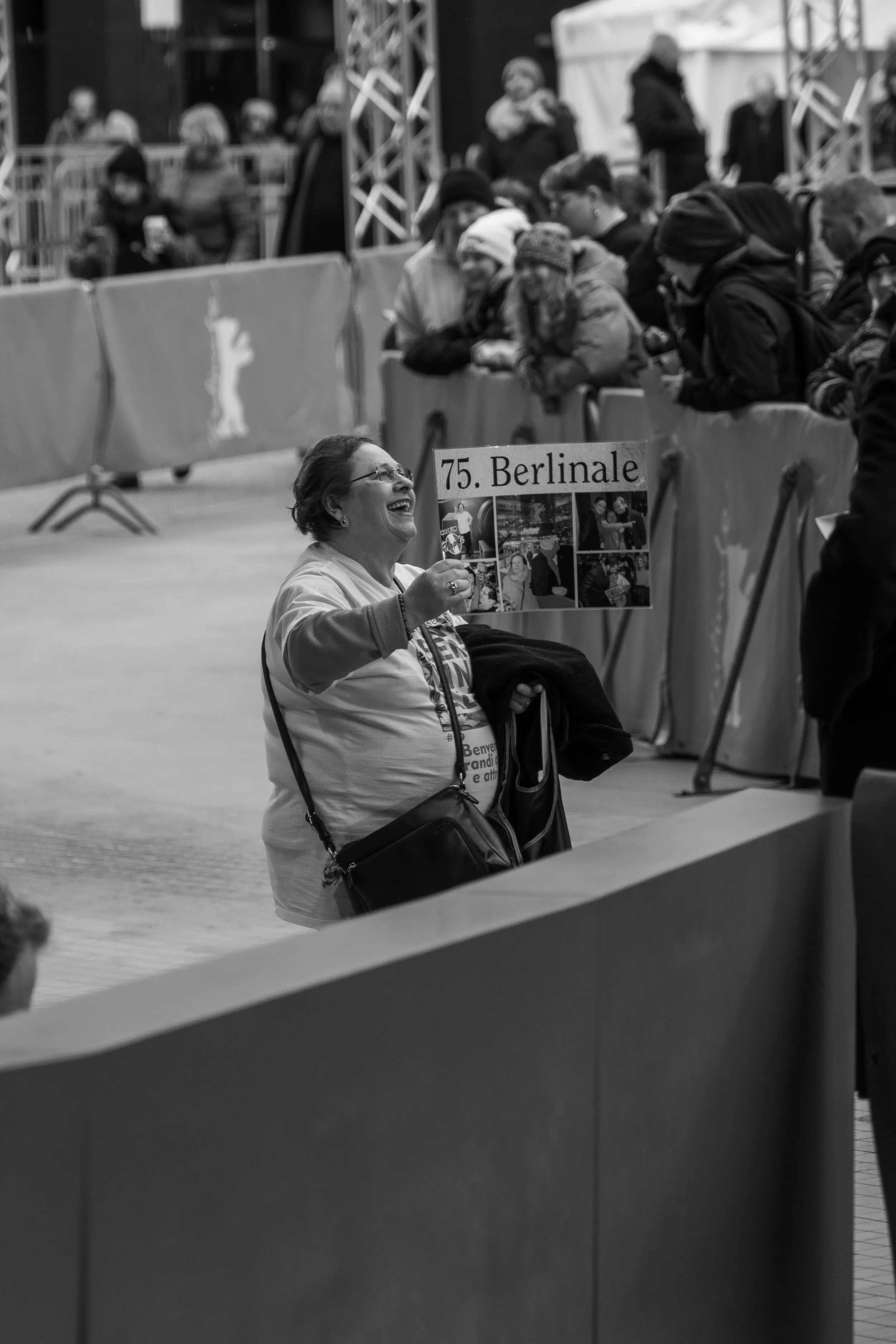 Frau hält ein Plakat mit der Aufschrift „75. Berlinale“ inmitten von Menschen in einer Warteschlange.