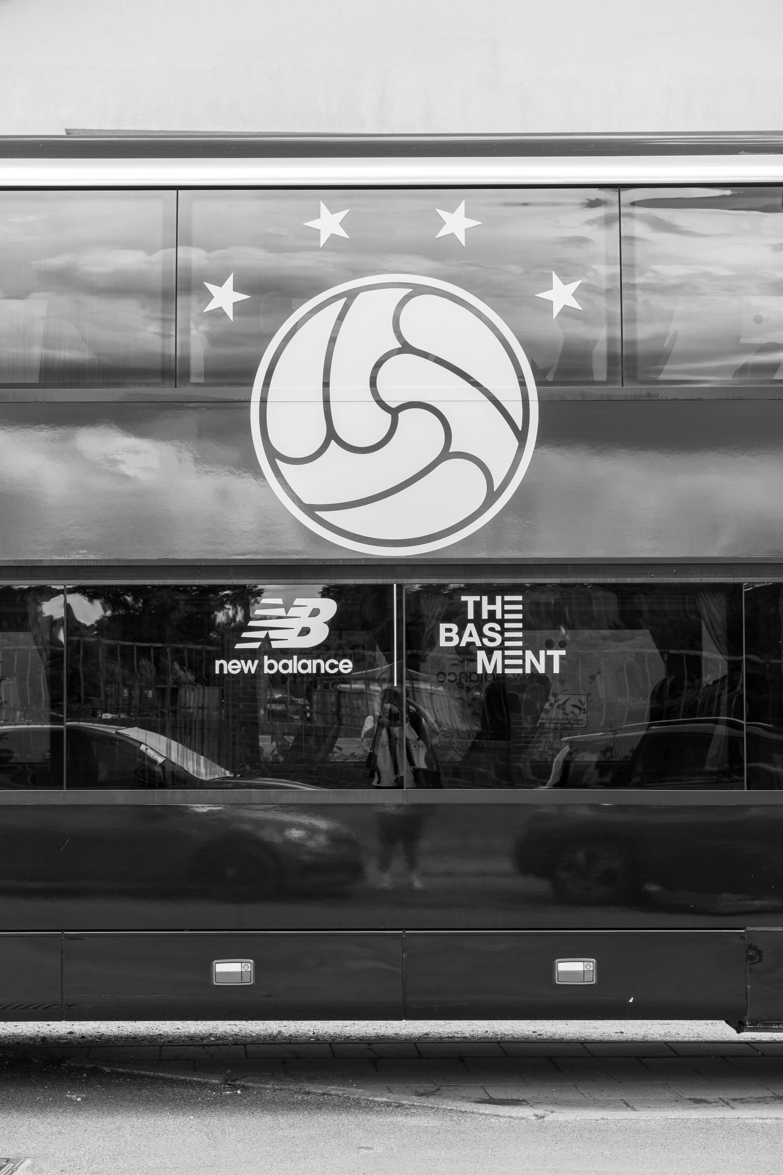 Seitenansicht eines Busses mit Logos von New Balance und The Basement. Oben ist ein großes Symbol mit Sternen zu sehen.