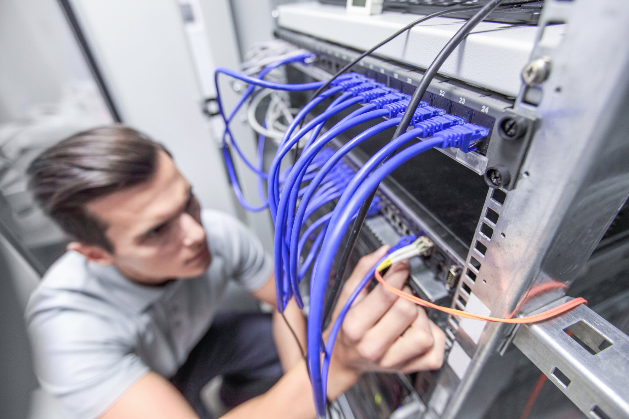 A man working on a server rack with multiple blue Ethernet cables connected to the hardware.