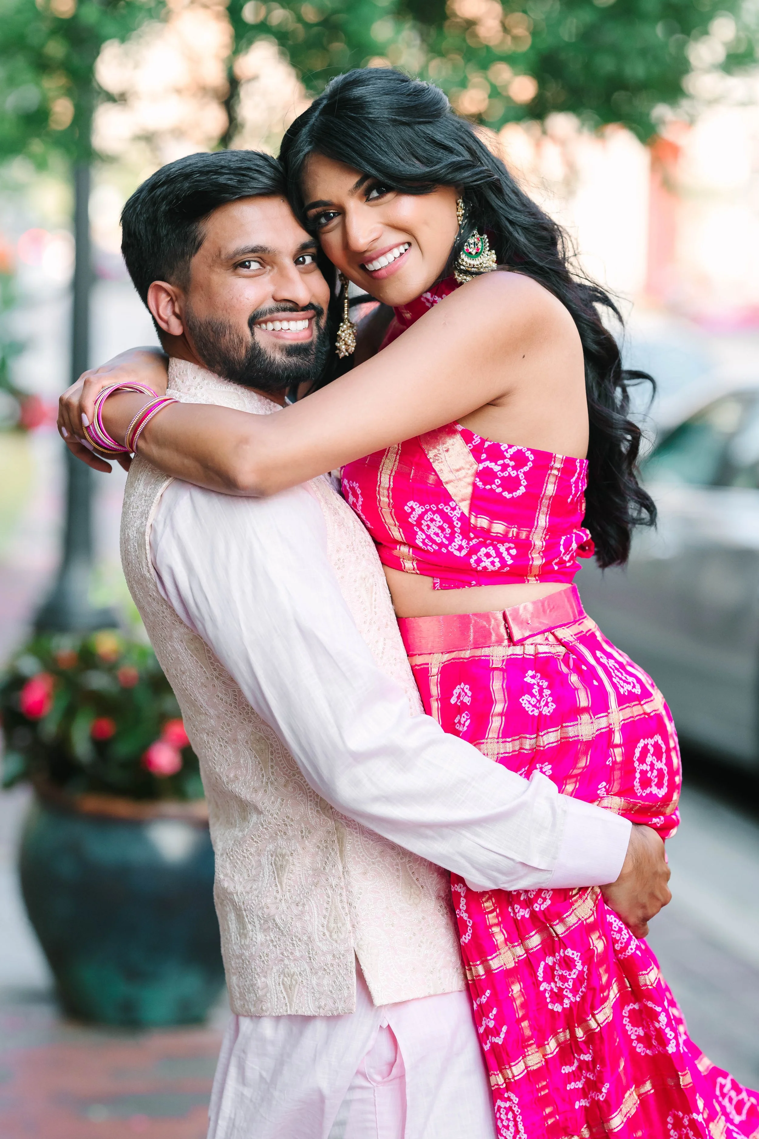 A couple embracing outdoors, smiling, with a colorful background and city street scene.