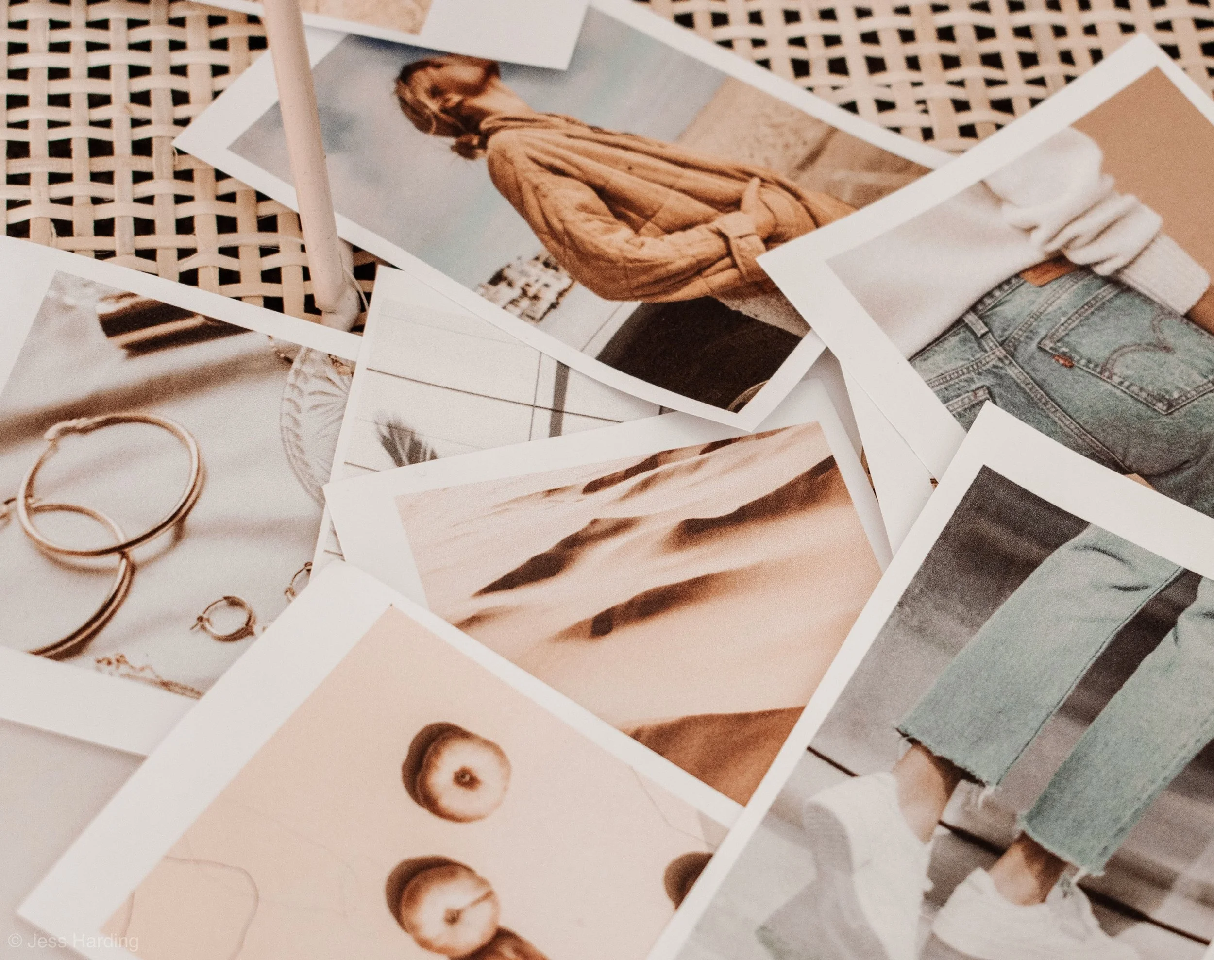 A collection of printed photographs and jewelry on a woven surface. The photos include a woman in a tan sweater, desert dunes, and a woman sitting with ripped jeans and white sneakers.