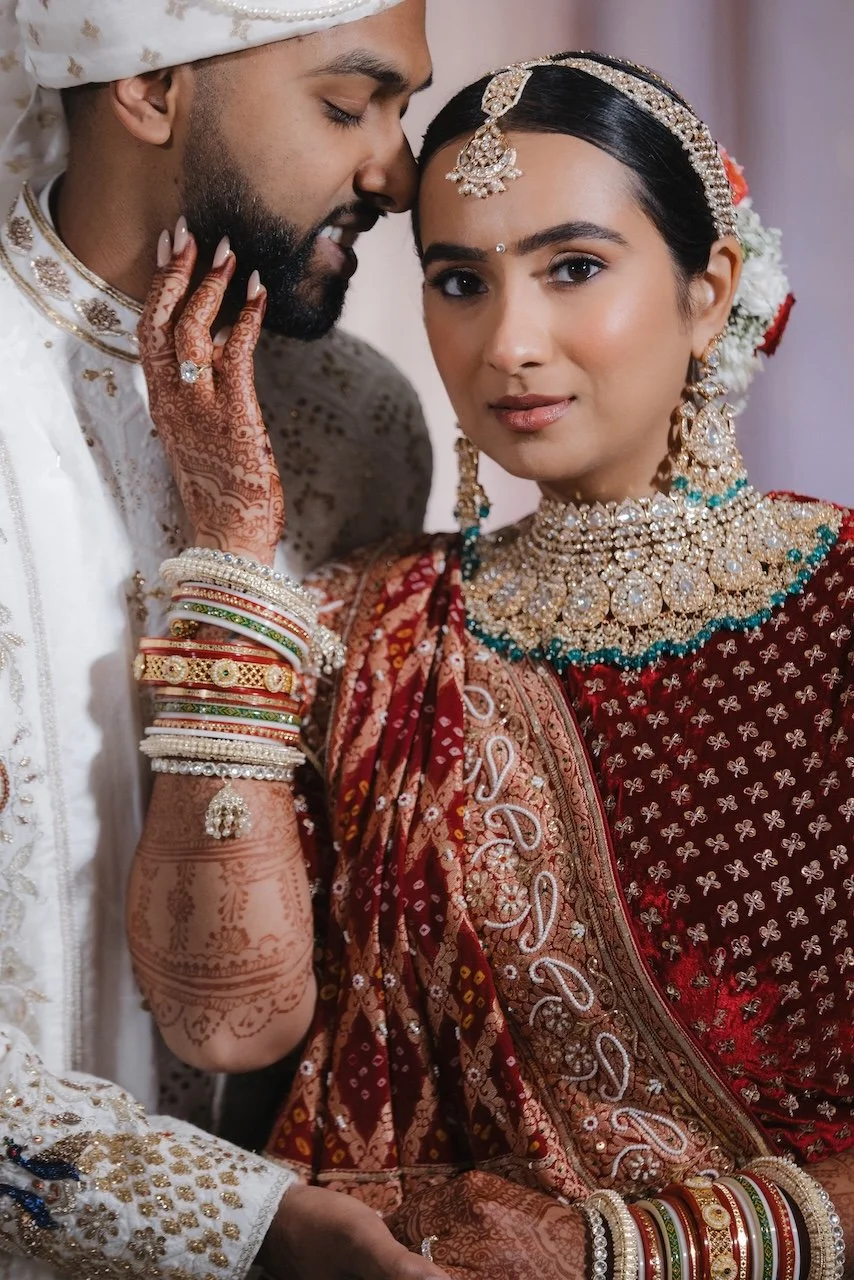 Indian bride and groom in traditional wedding attire, with the groom gently touching the bride's face.