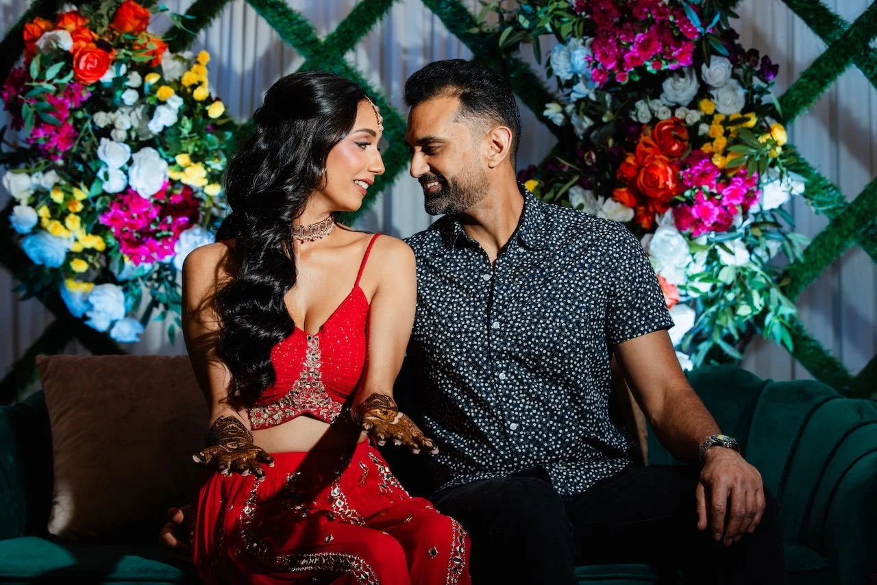 A couple sitting close together on a sofa during a celebration, with colorful flower arrangements in the background.