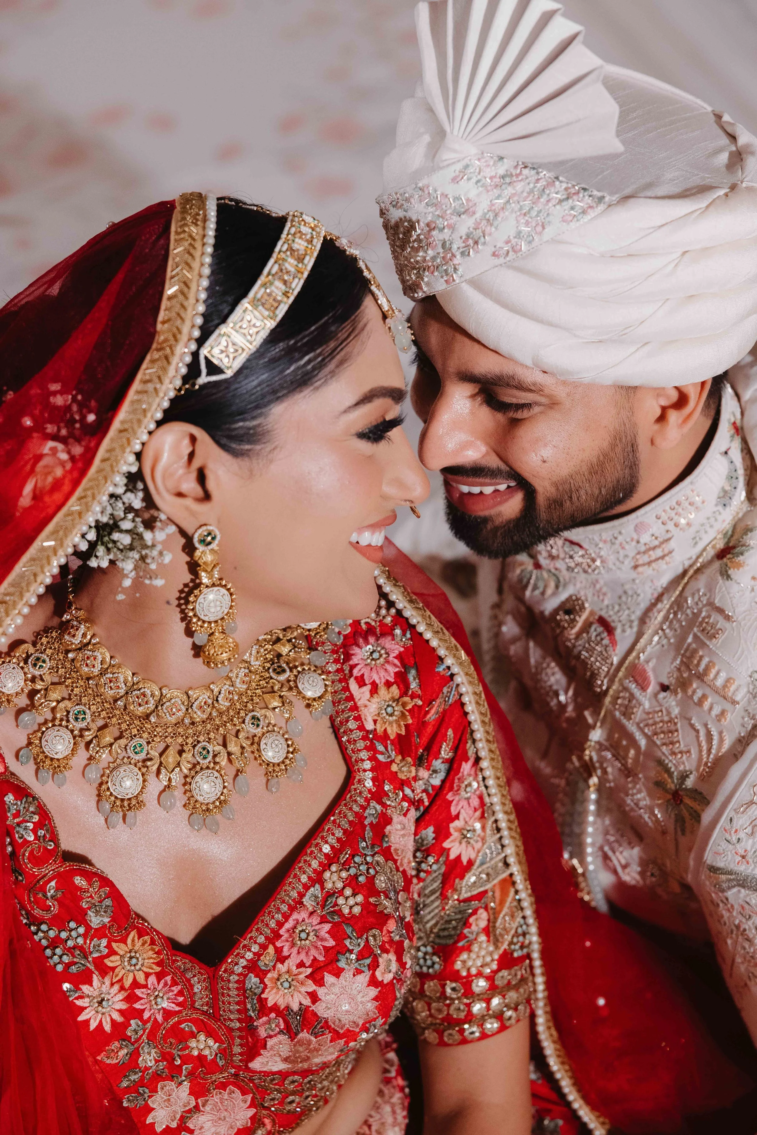 Close-up of a smiling bride and groom in traditional Indian wedding attire, touching foreheads.