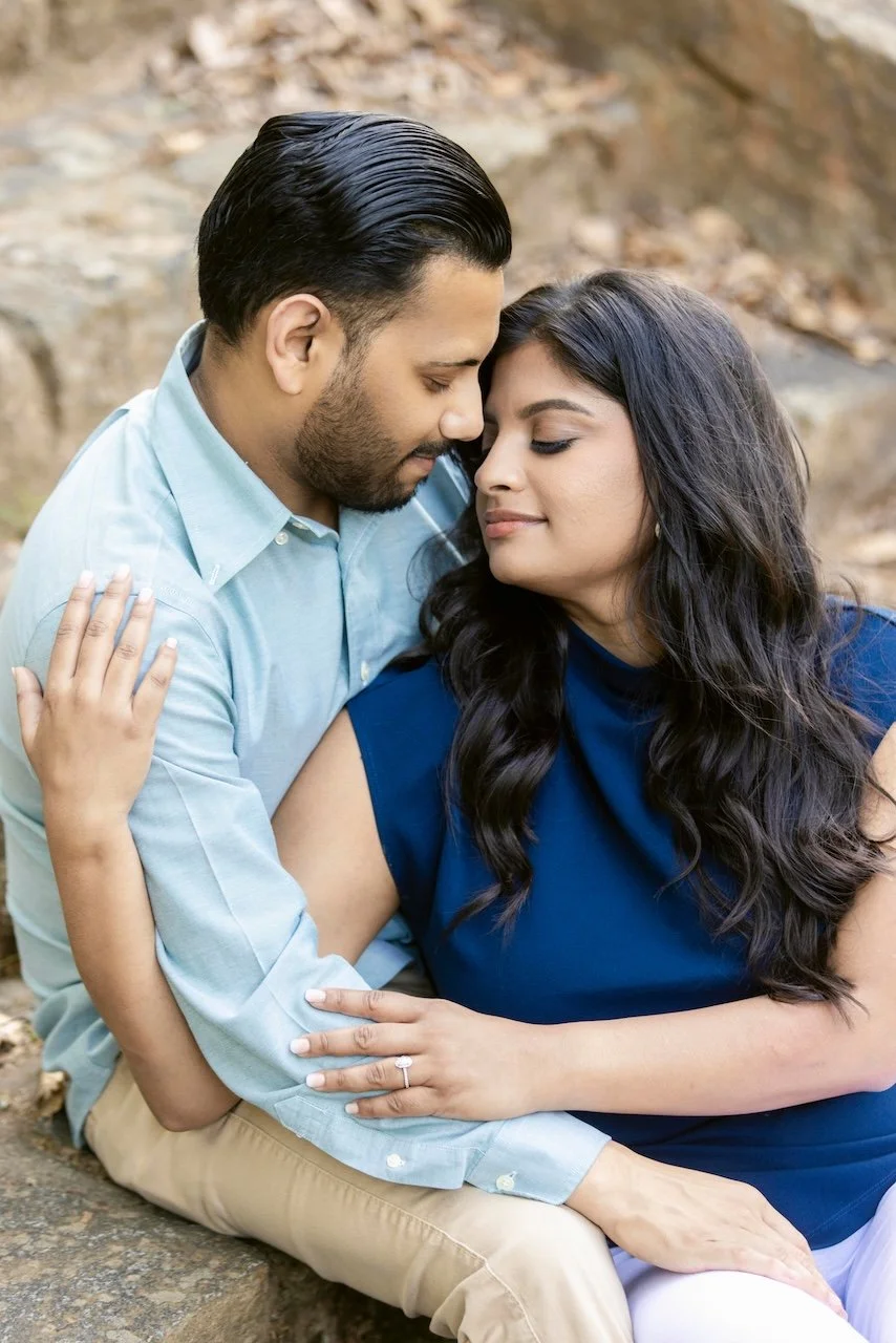 A couple sitting outdoors on a rock, embracing and touching foreheads with eyes closed.