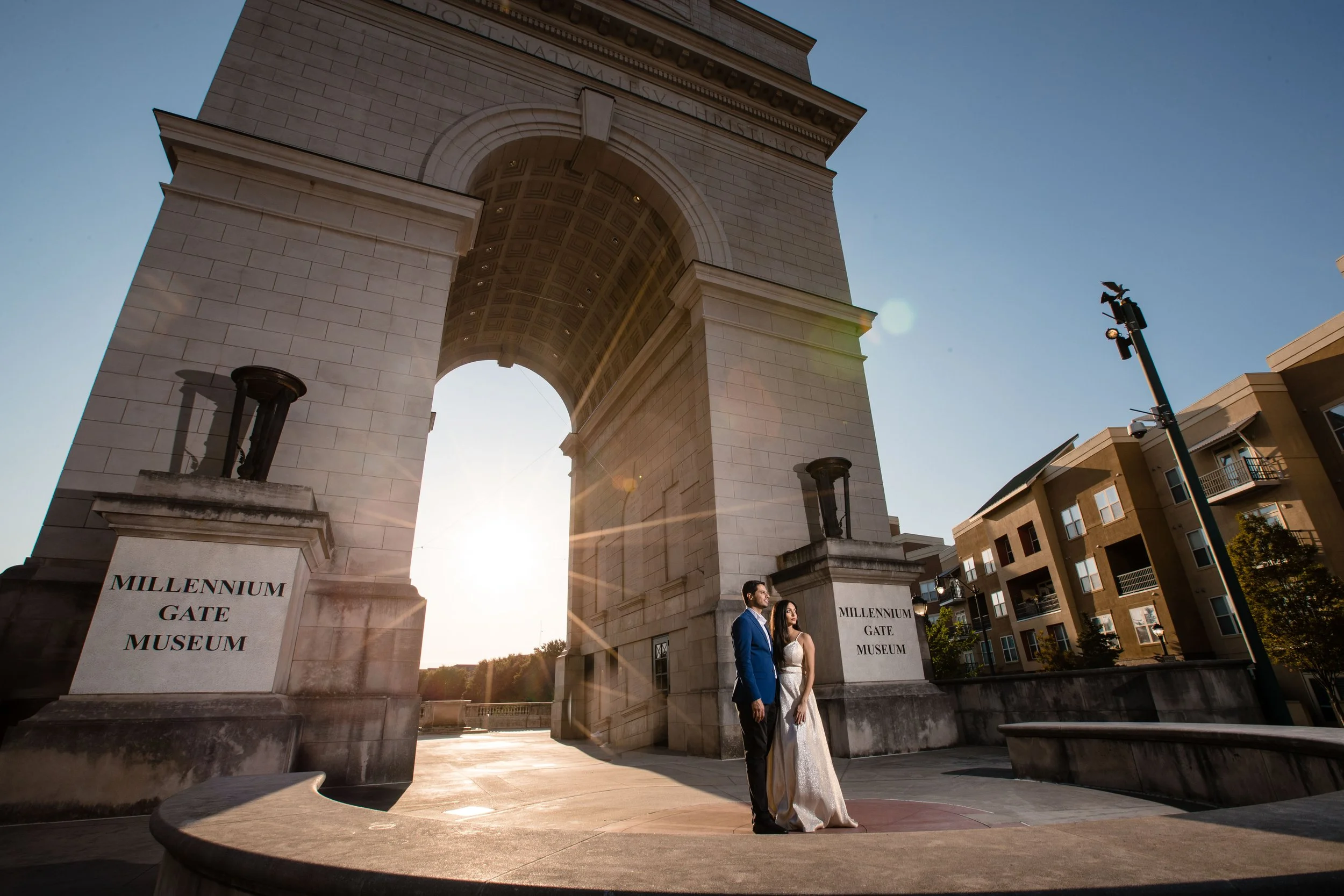 A couple dressed in formal attire standing in front of the Millennium Gate Museum at sunset.