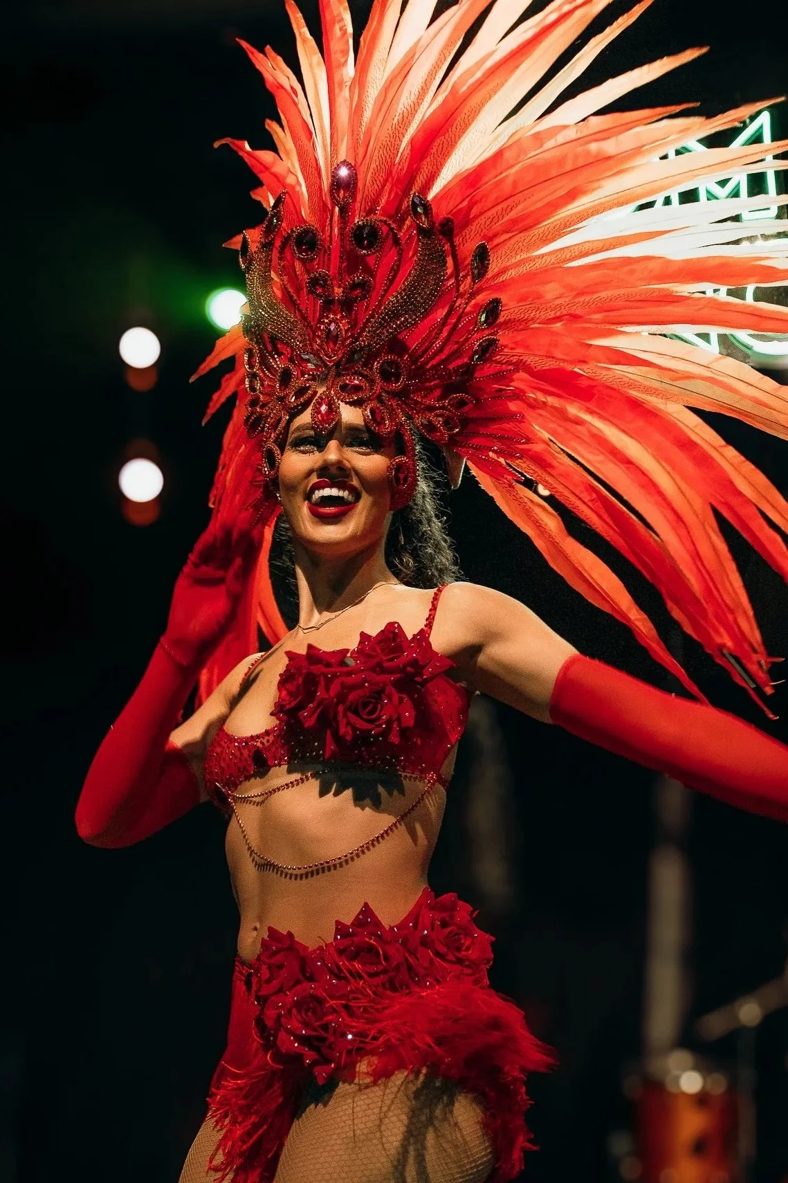 A woman in a vibrant red carnival costume with a large feathered headpiece, smiling and posing at a festive event.