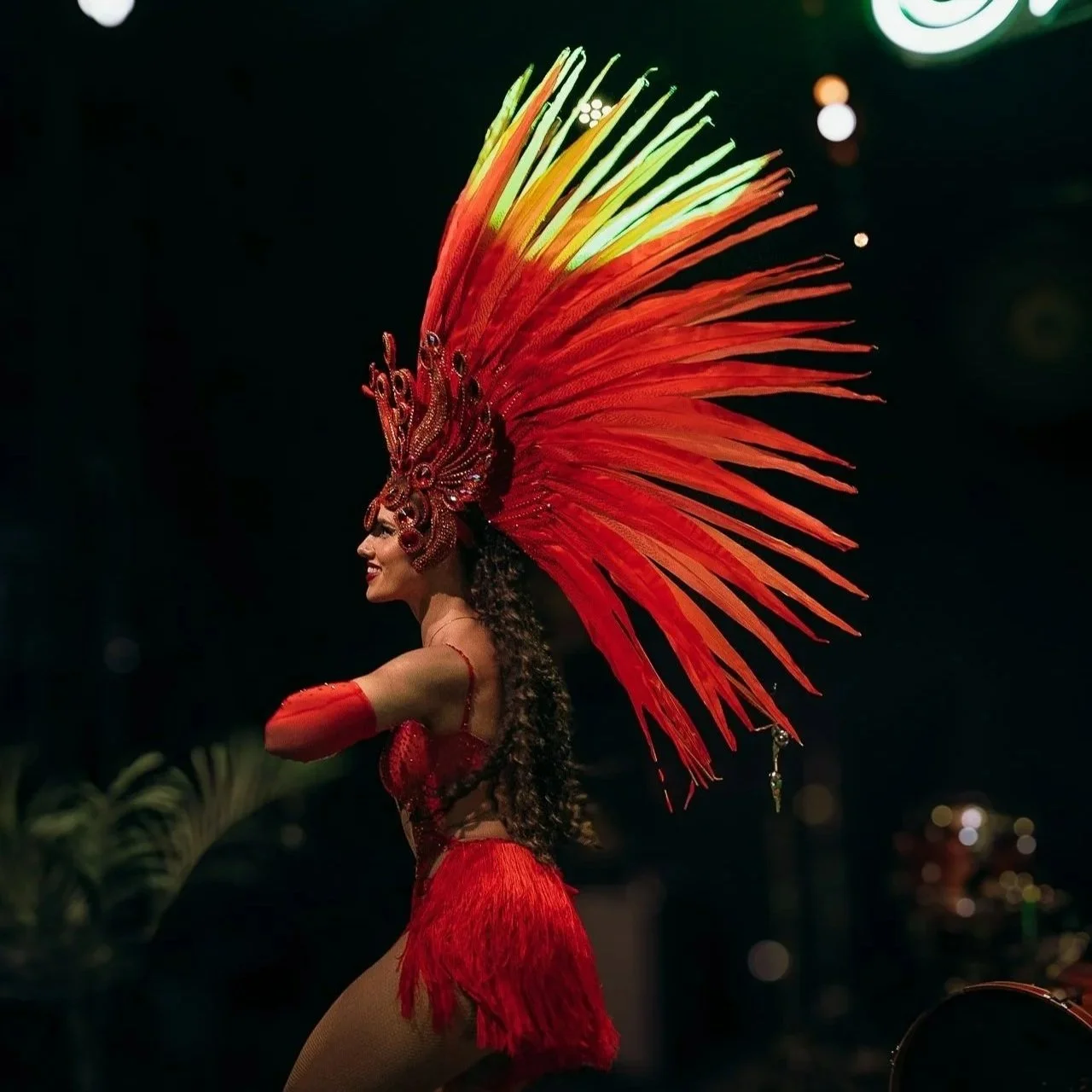 A woman in a red costume with an elaborate feathered headdress performing a dance or participating in a cultural event.