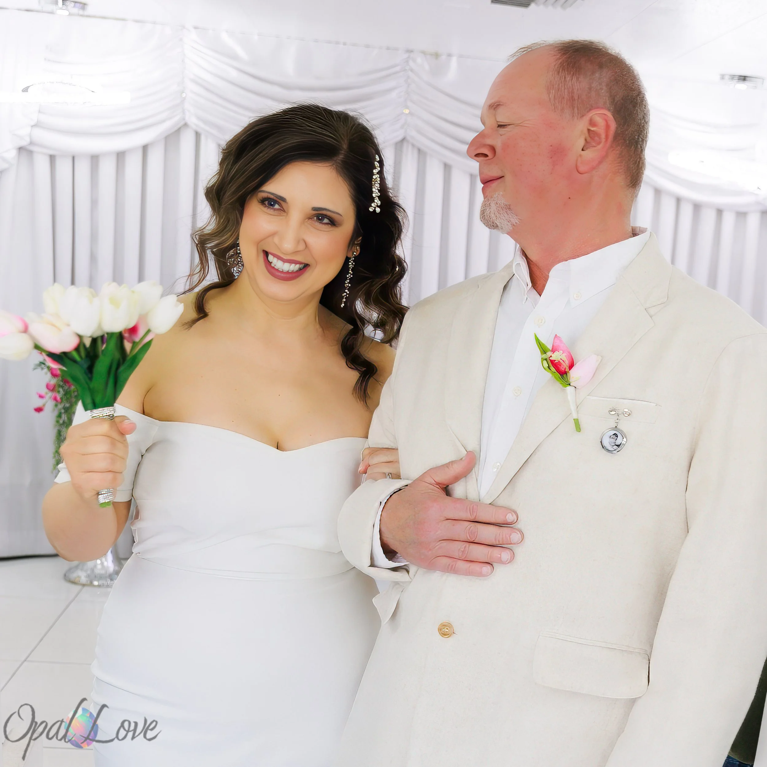 Bride holding a bouquet and smiling while standing arm in arm with a man in a cream suit.