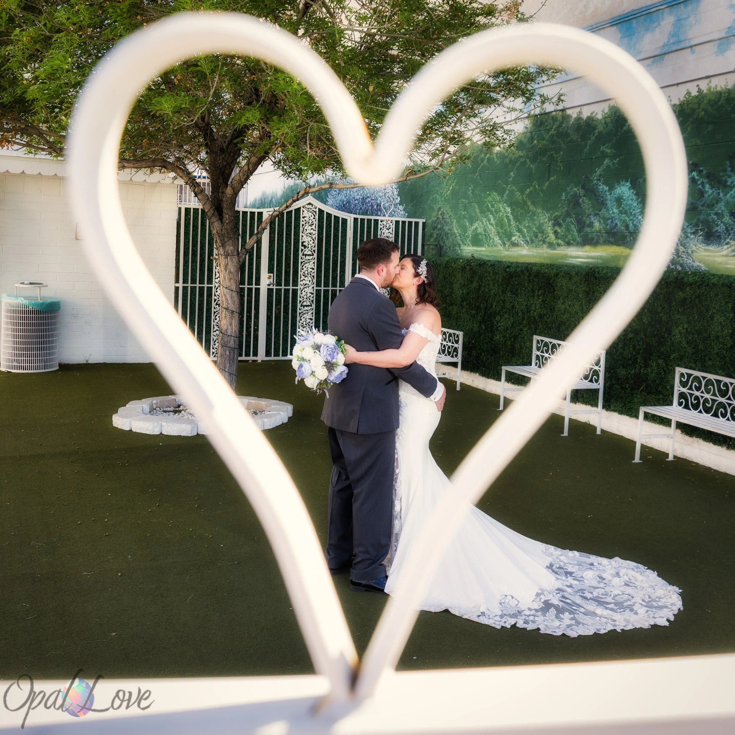 Bride and groom kissing in a garden framed by a heart shaped arch at their Las Vegas wedding chapel.