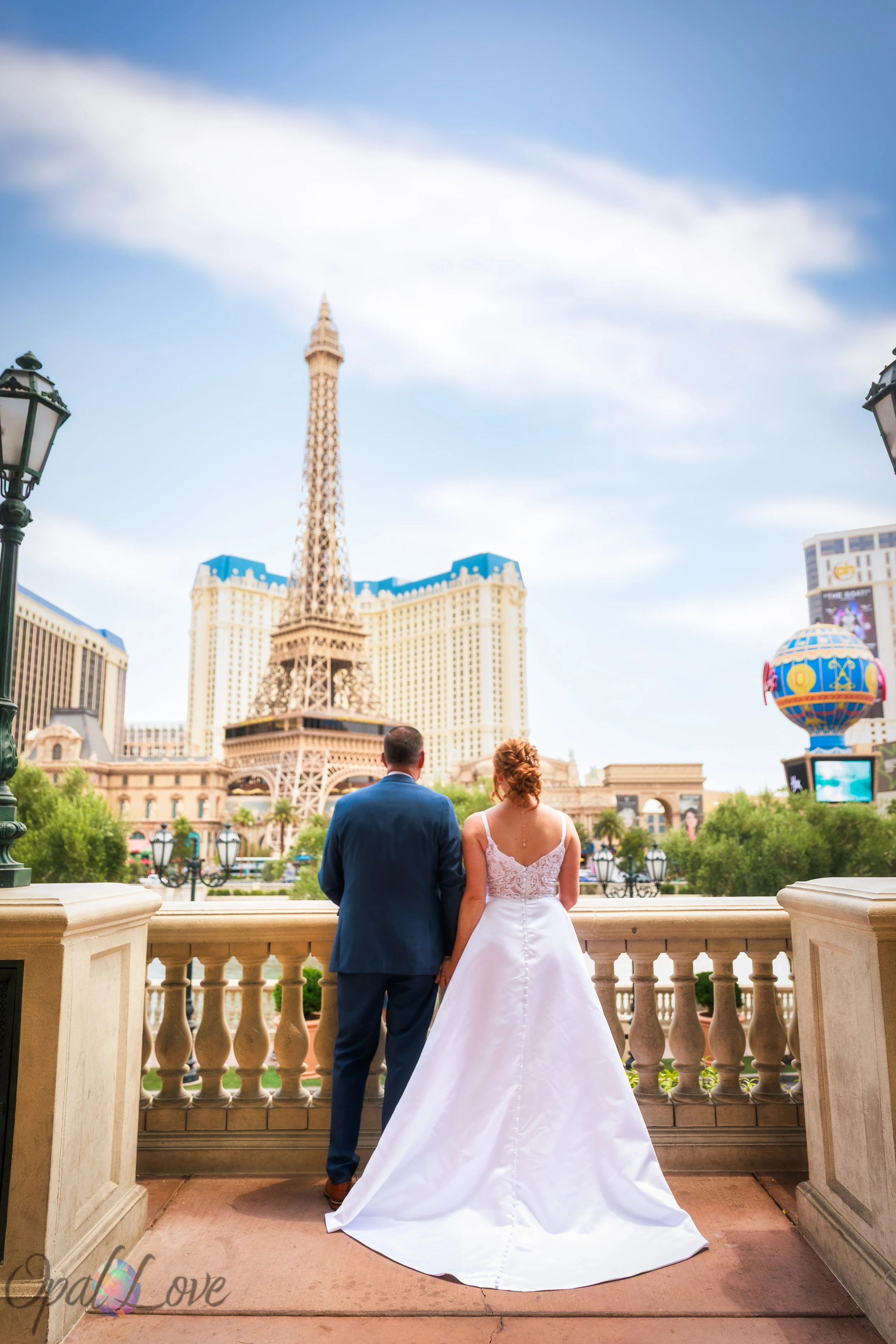 Bride and groom standing together at the Bellagio terrace with the Eiffel Tower view in the background captured by Opal Love Photography.
