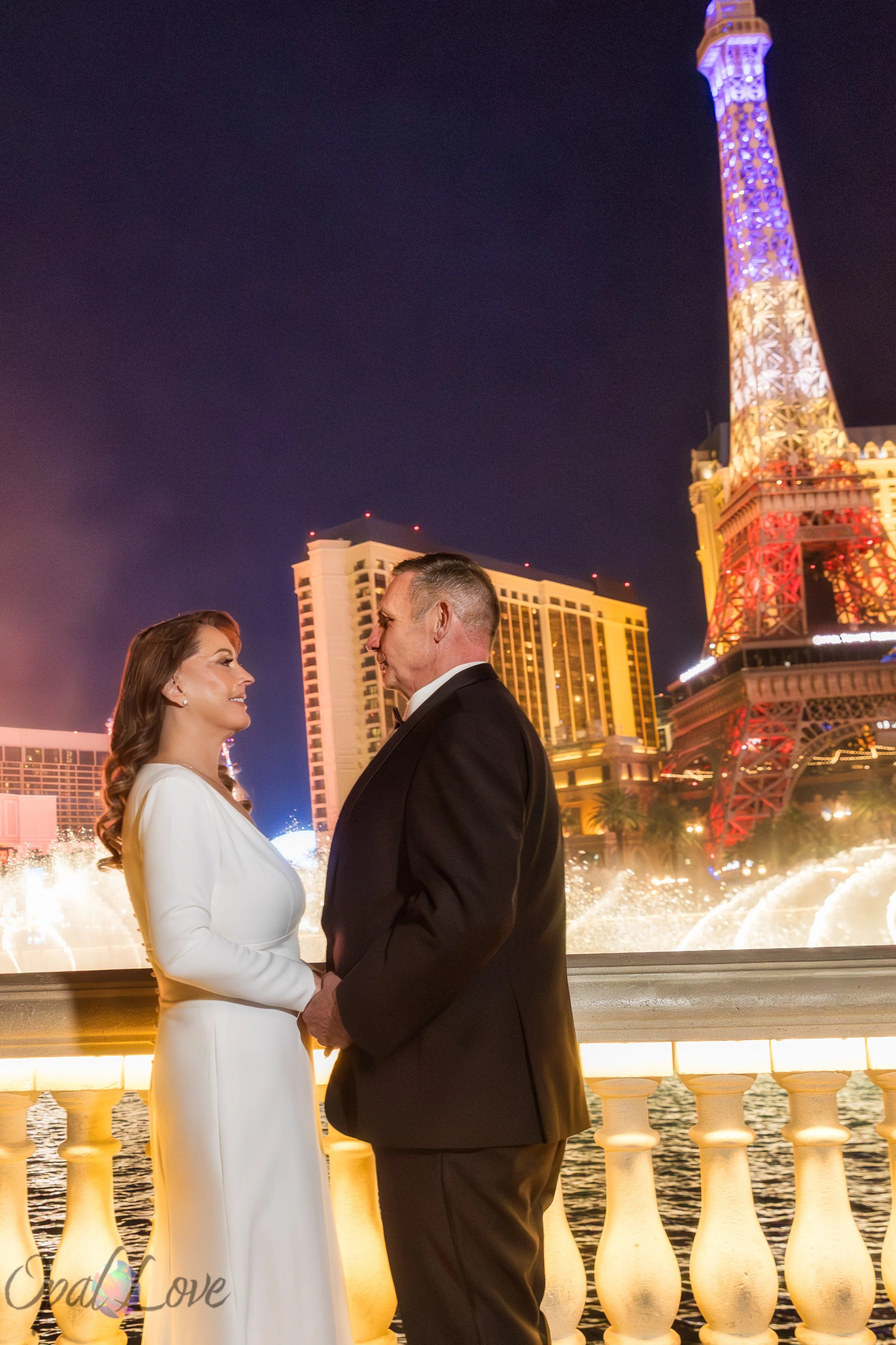 Couple facing each other at Bellagio with Eiffel Tower and Strip lights behind them