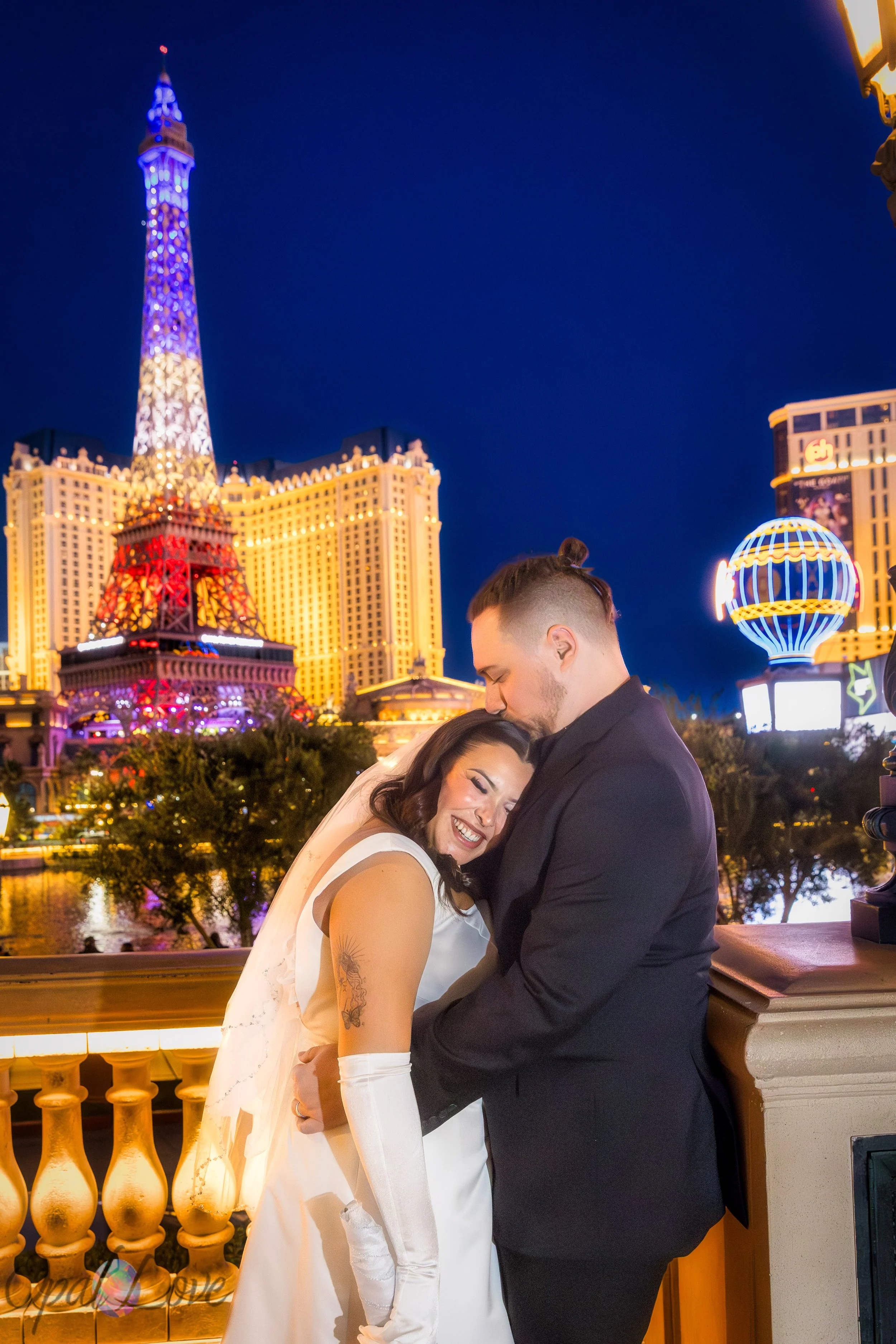 Couple embracing along the Bellagio railing with bright Strip lights behind them.