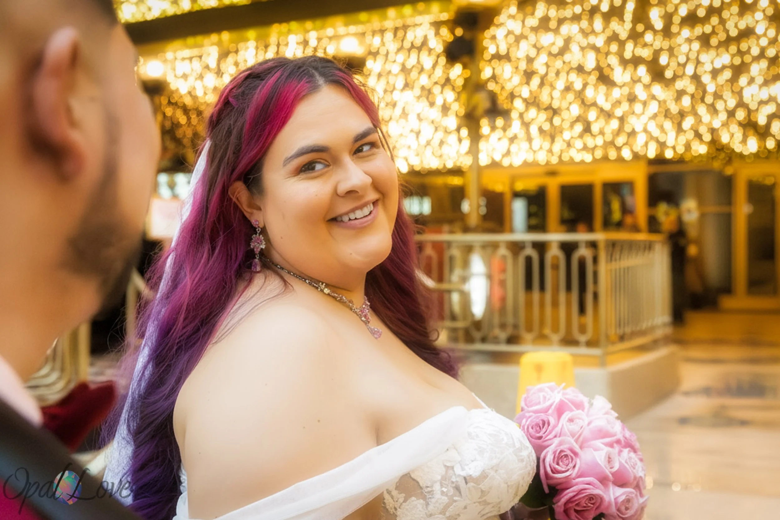Bride smiling over her shoulder with golden marquee lights behind her.