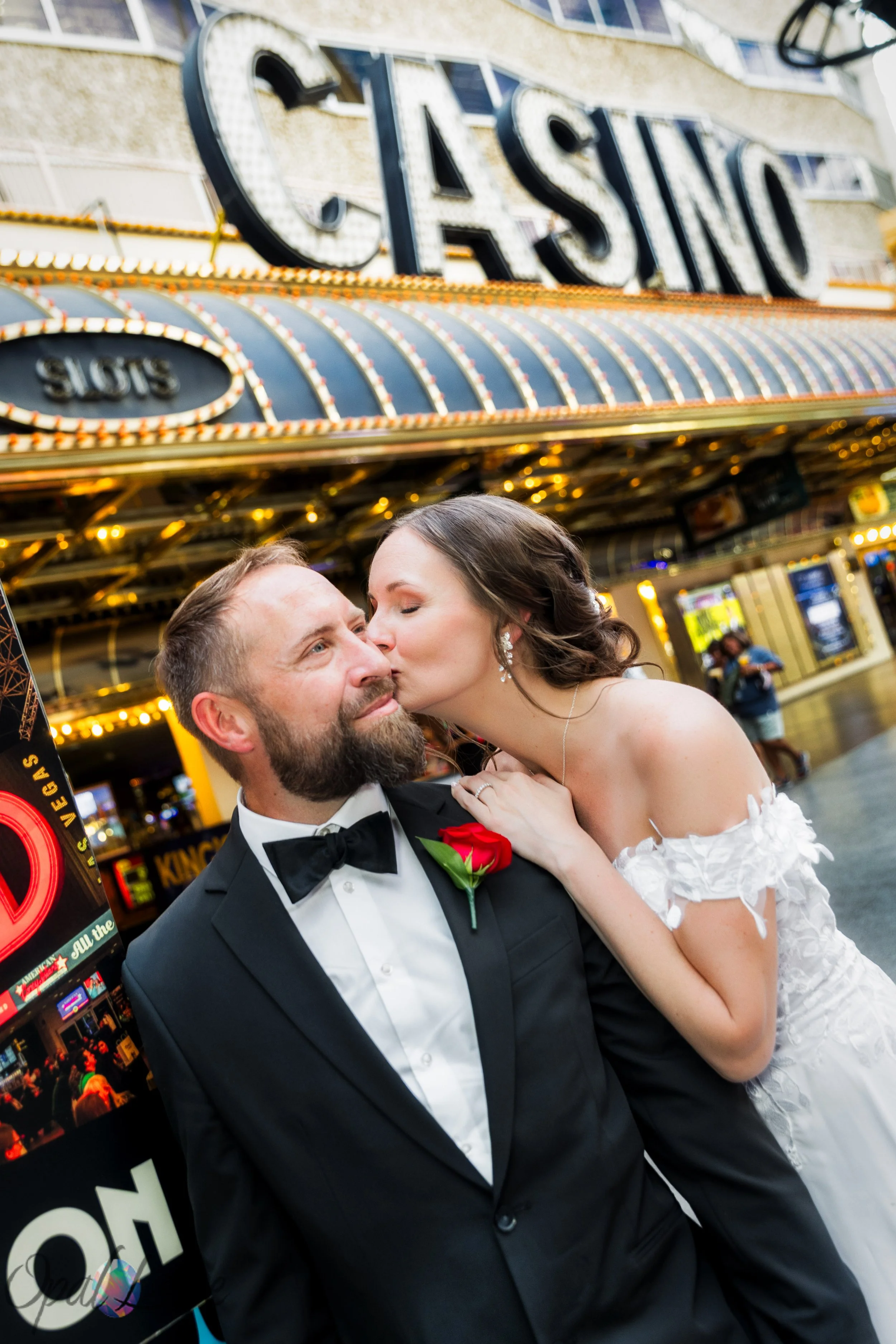 : Kari kissing Rickie beneath a classic Fremont Street casino marquee during their Downtown Las Vegas wedding photos.