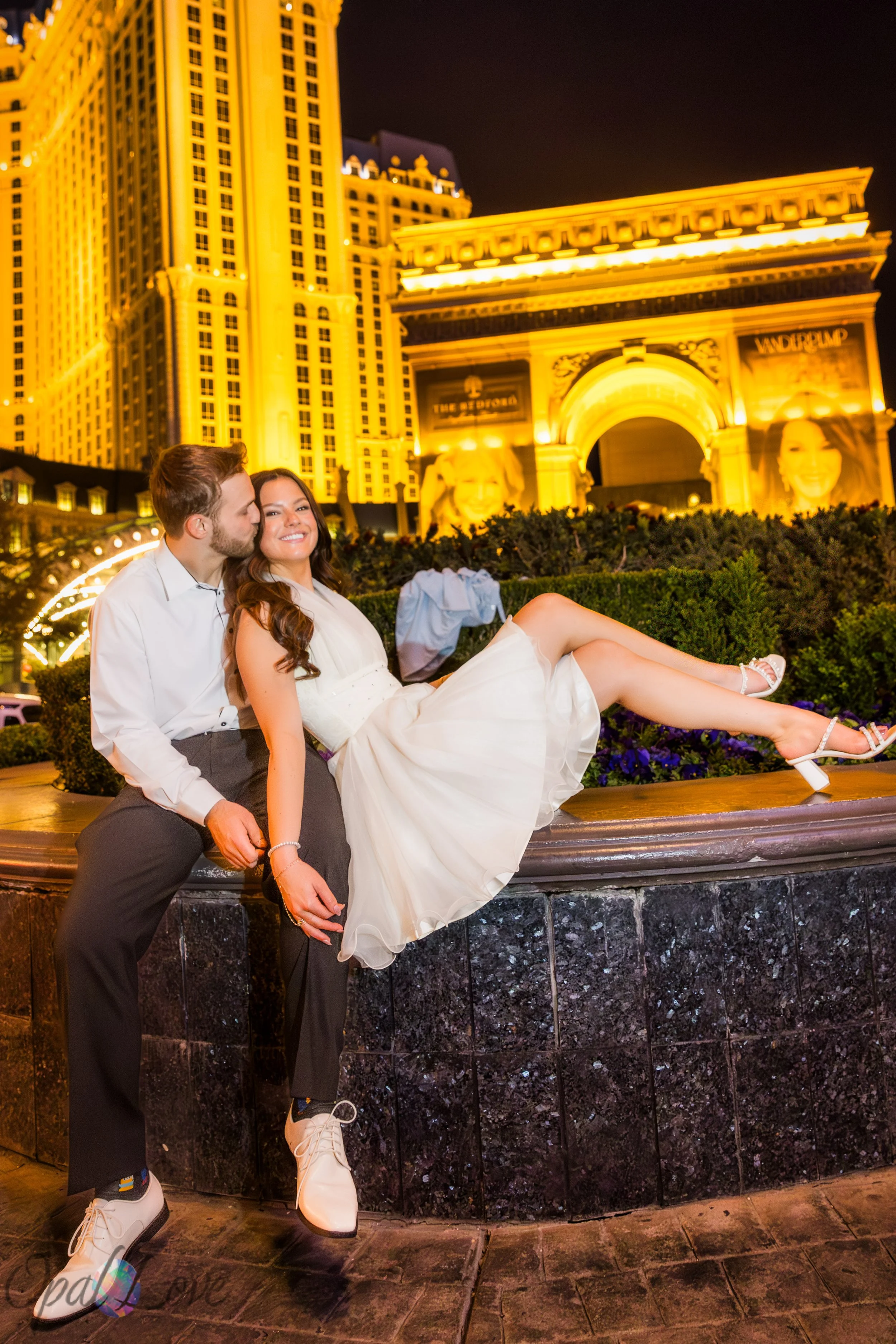 Bride and groom sitting together at Paris Las Vegas with the glowing hotel lights behind them during their Las Vegas elopement photo tour.