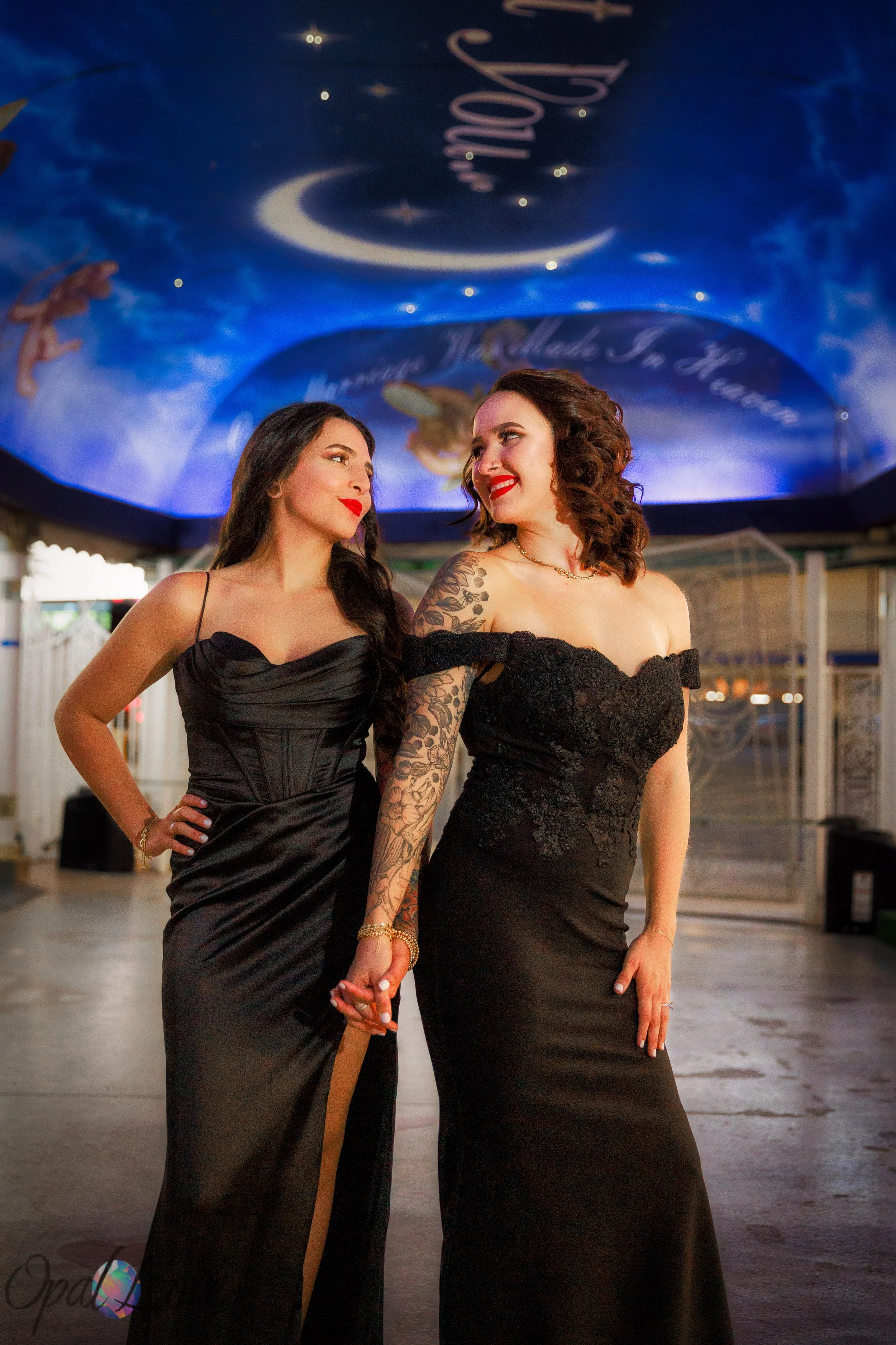 

Couple in black gowns holding hands beneath a blue ceiling painted with stars and cherubs.