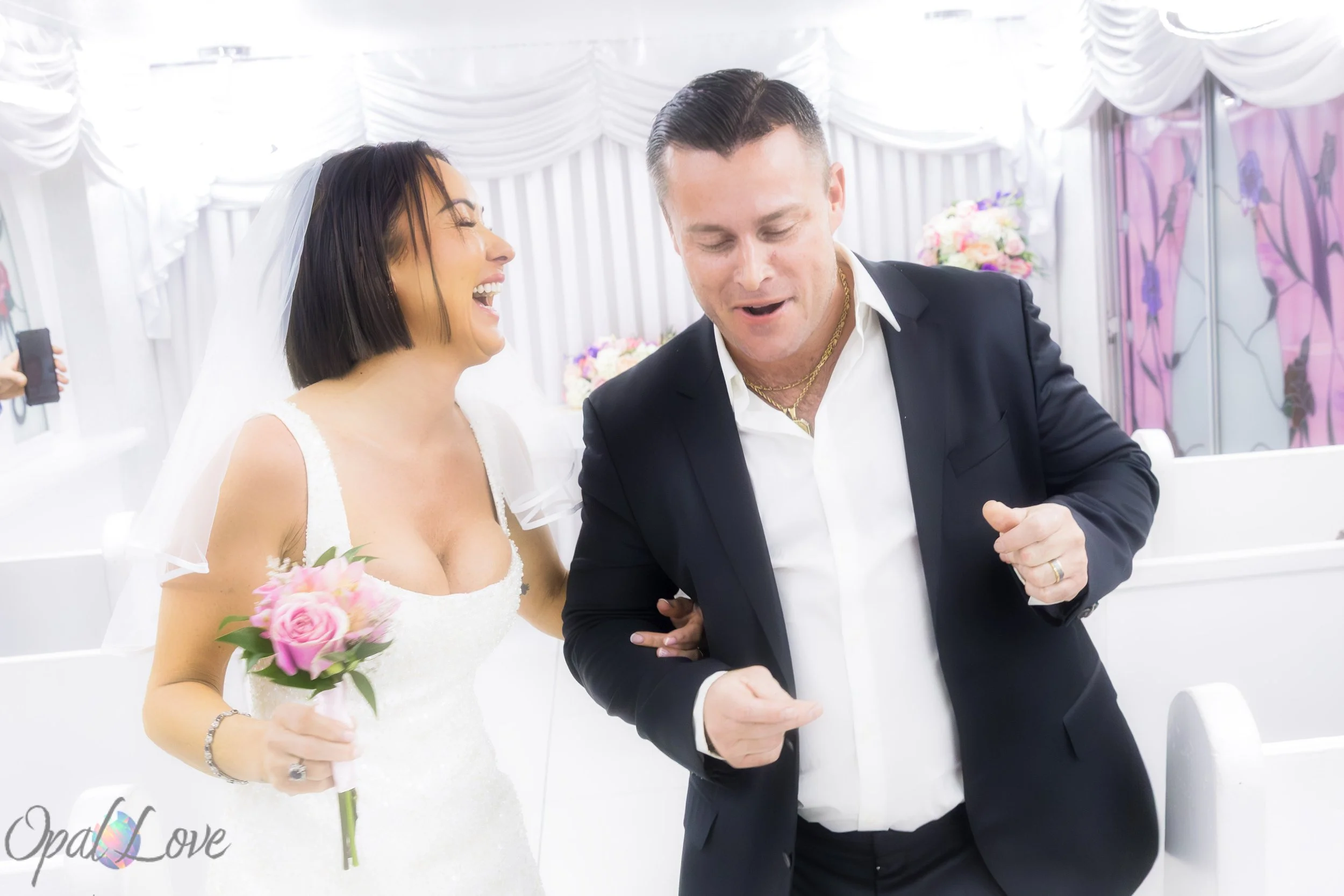 

Bride laughing beside her groom as they celebrate in a white wedding chapel.