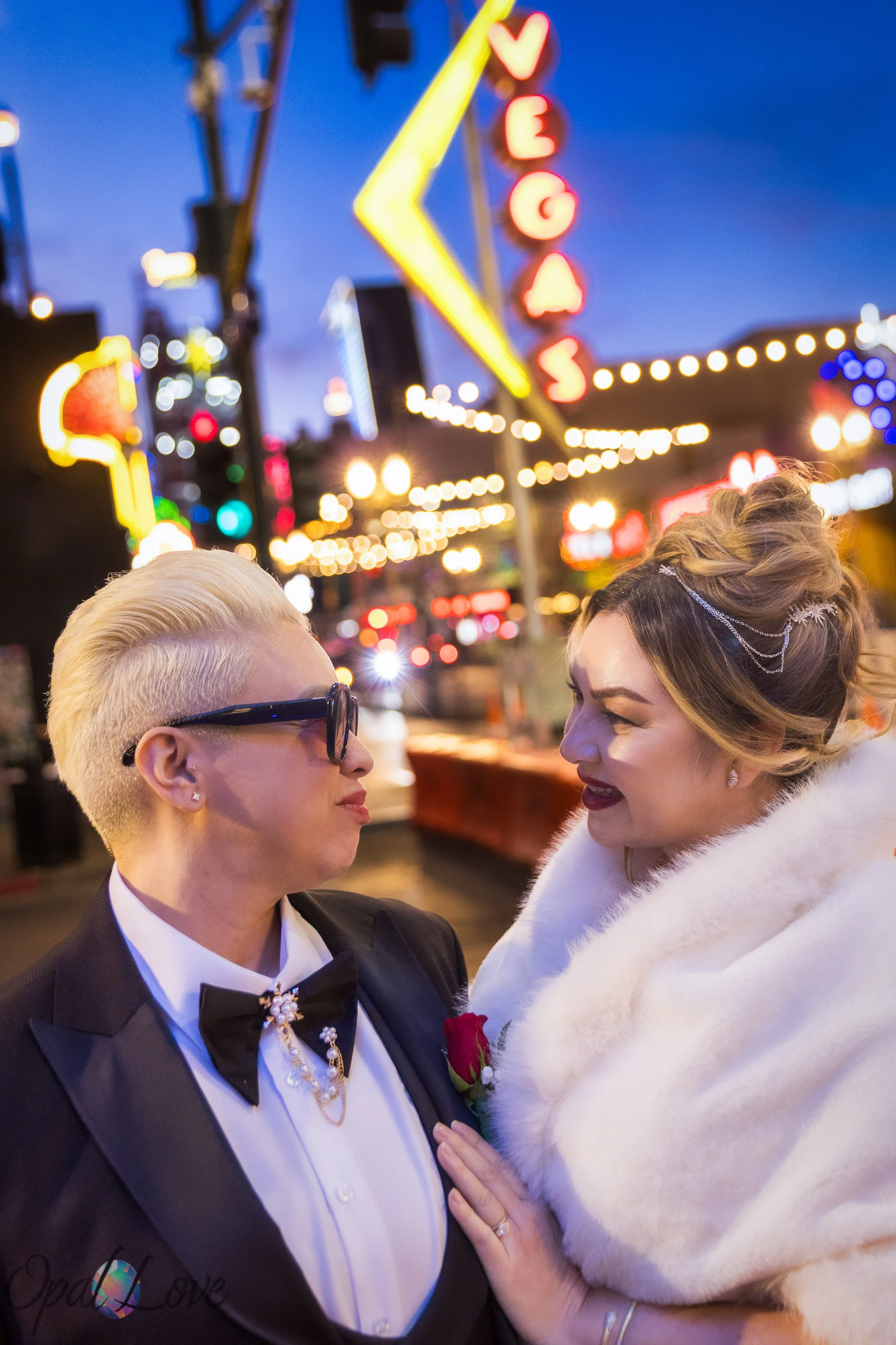 Couple standing close together on Fremont Street with vintage Vegas neon signage lighting the background.