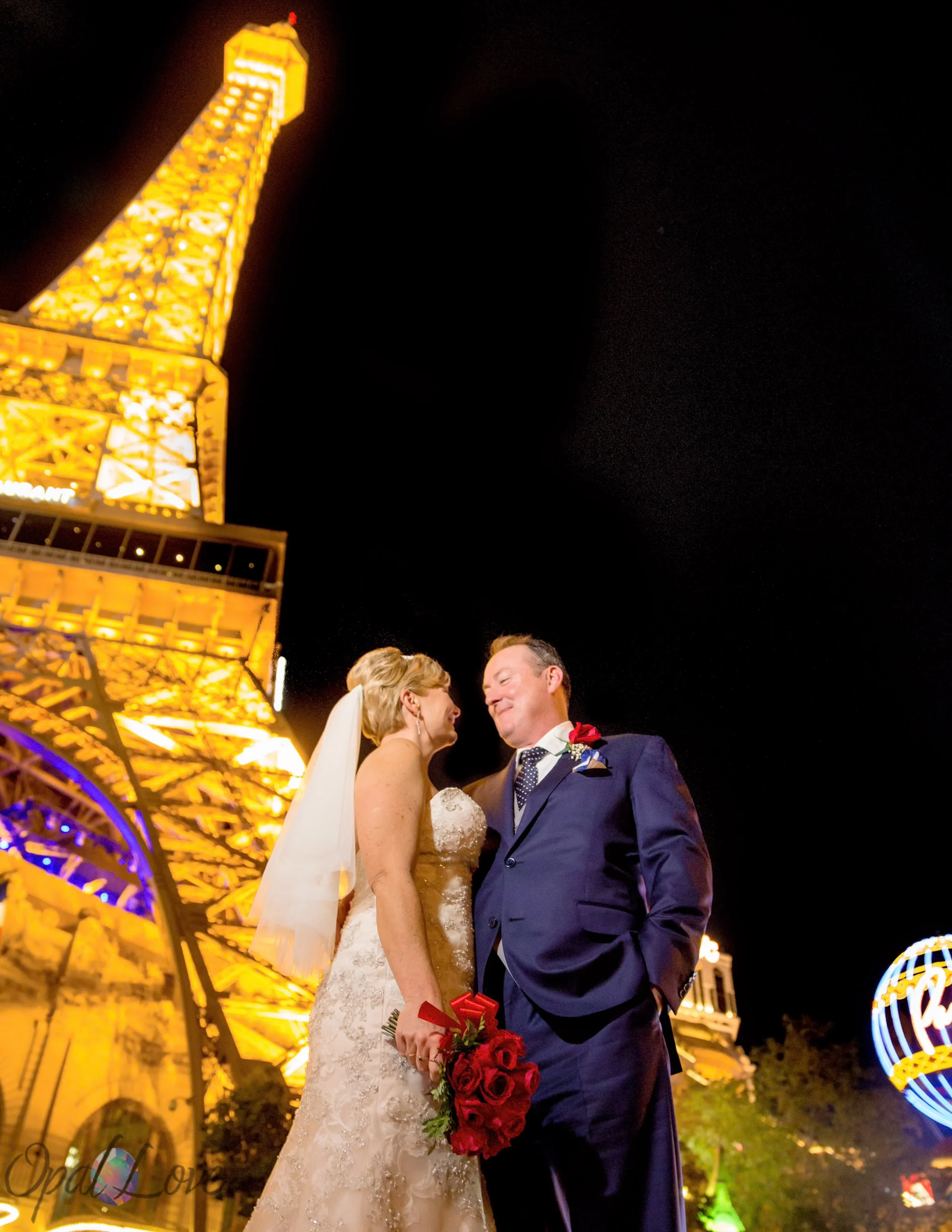 Newlyweds pose beneath the illuminated Eiffel Tower at Paris Las Vegas at night.