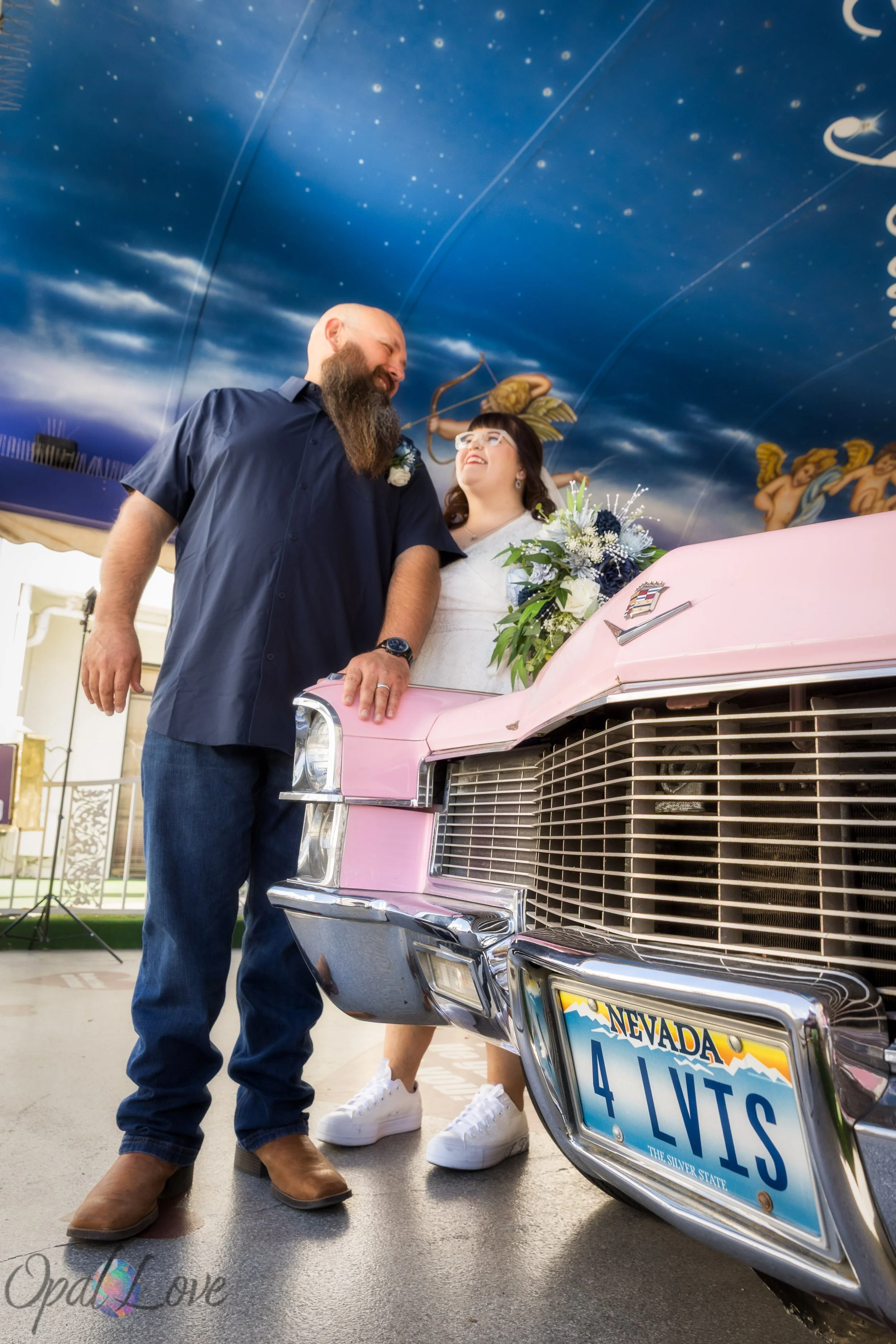 Couple standing beside the front of the pink Cadillac with the starry ceiling above them.