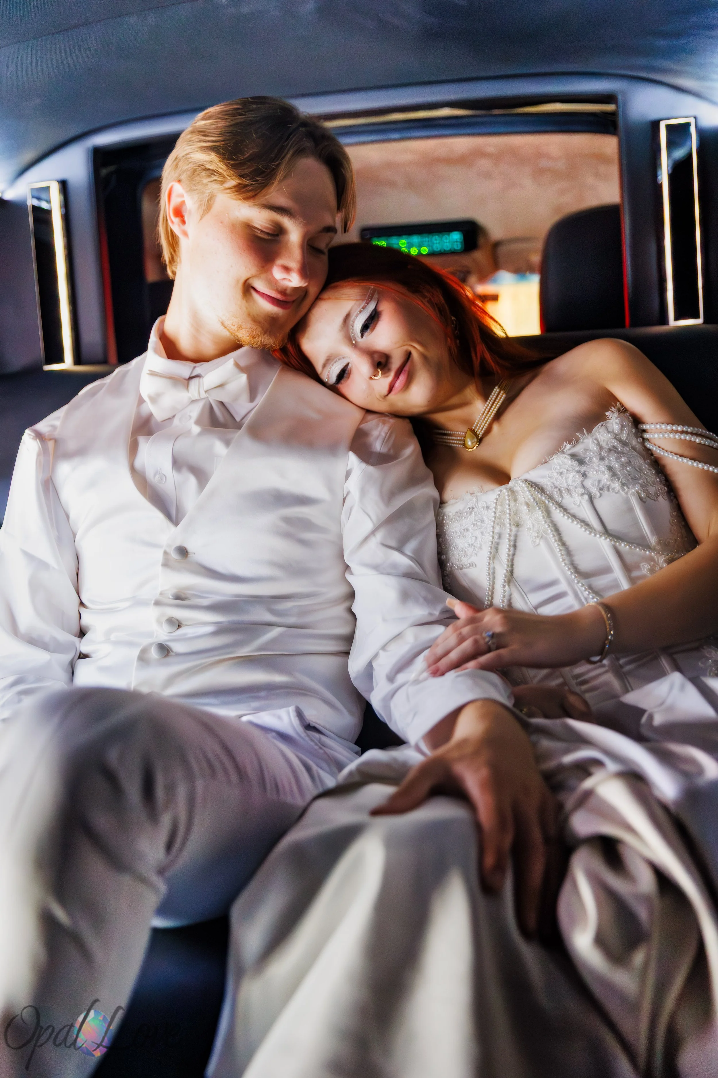 Couple holding hands in a limousine, with one resting their head on the other’s shoulder.