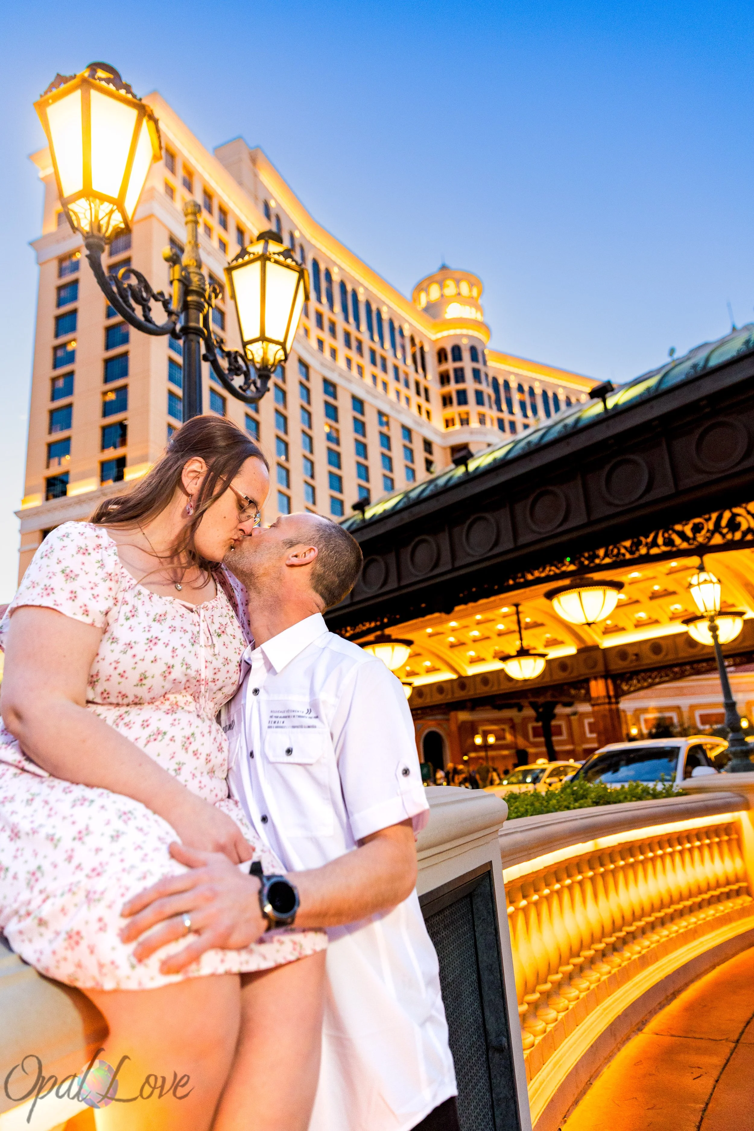 Couple kissing at Bellagio Las Vegas during a nighttime anniversary photo session with glowing hotel lights behind them.