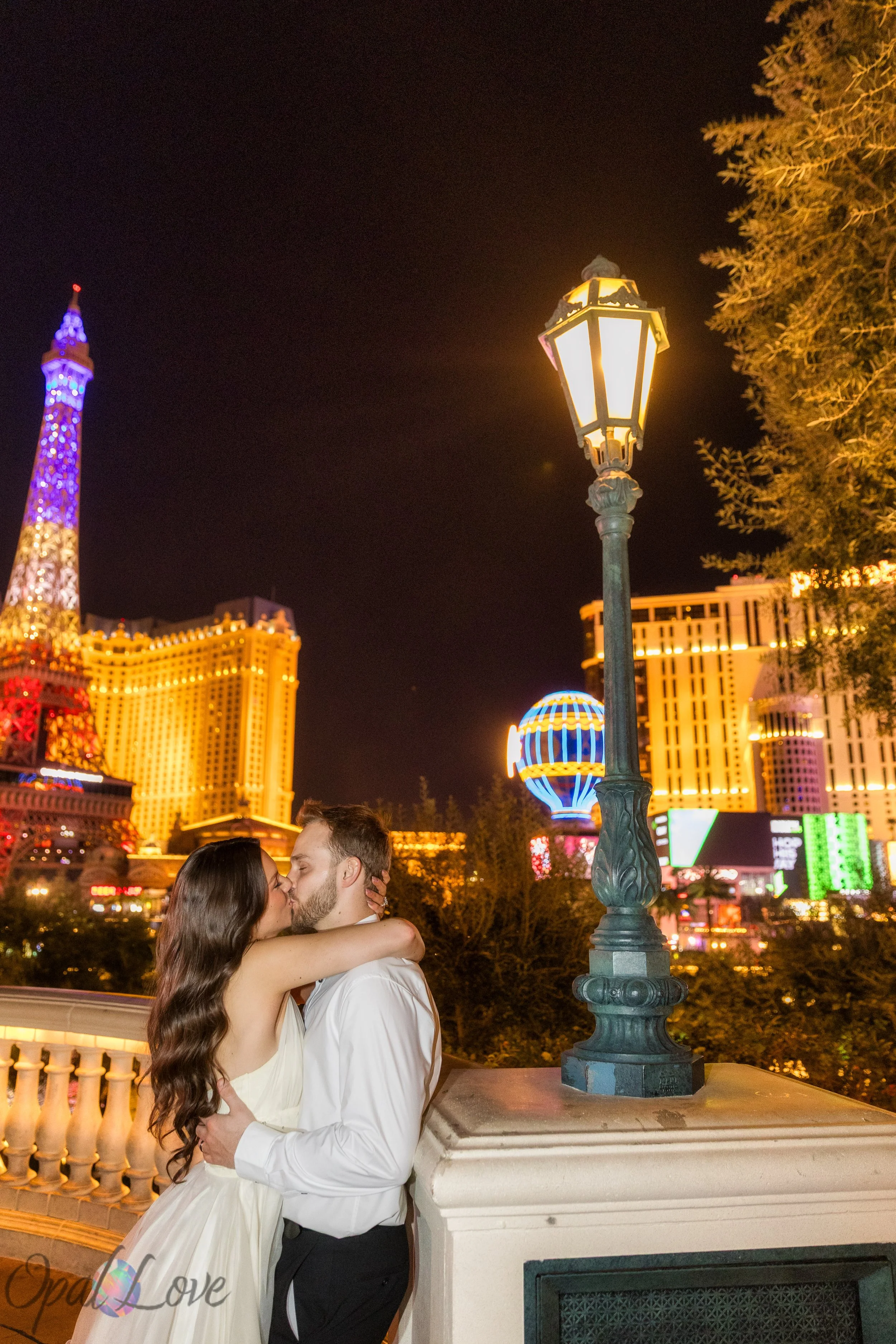 Newlyweds standing close together with Las Vegas Strip lights glowing behind them near Paris Las Vegas.