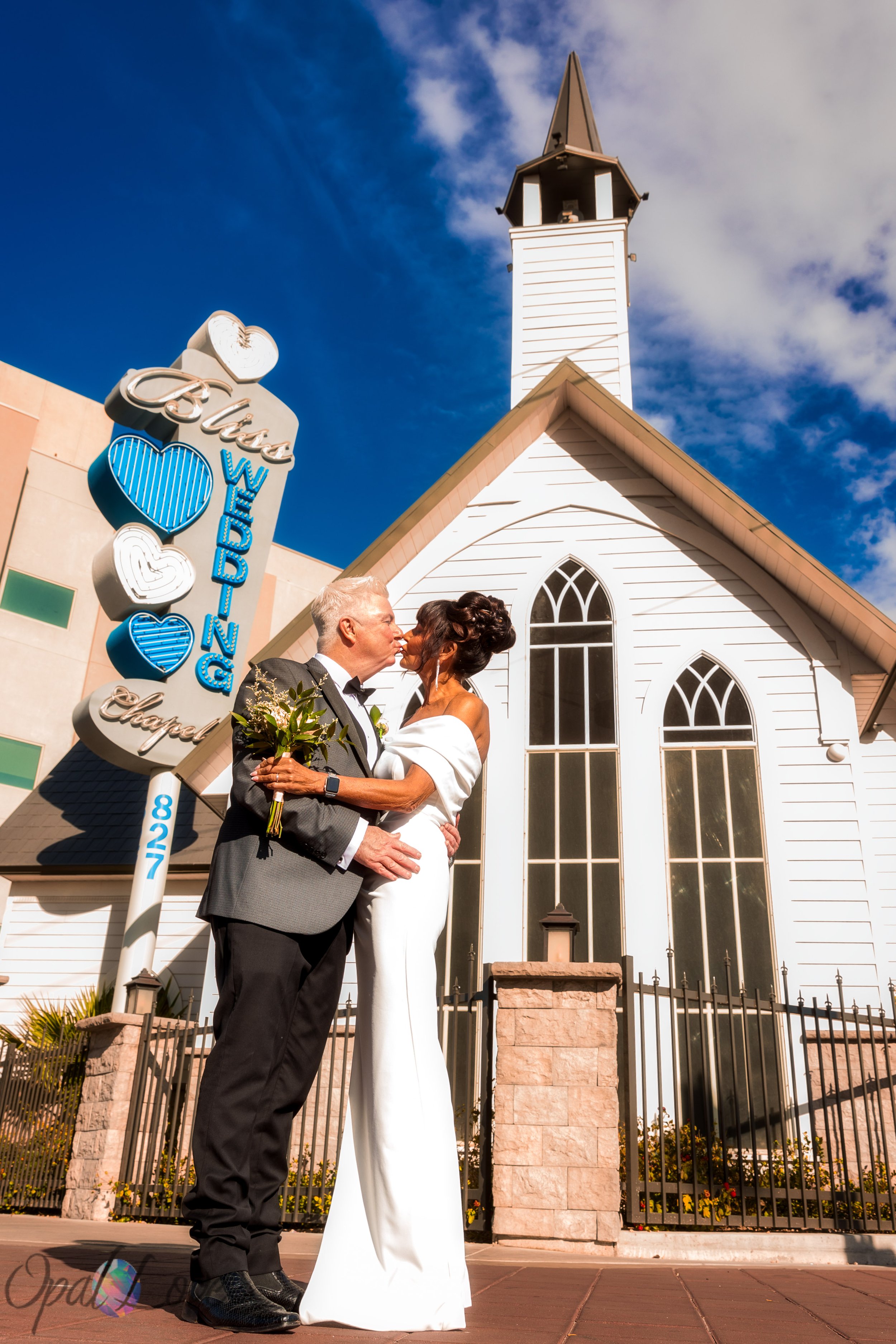 Newlyweds kissing outside a white chapel with a steeple and arched windows.