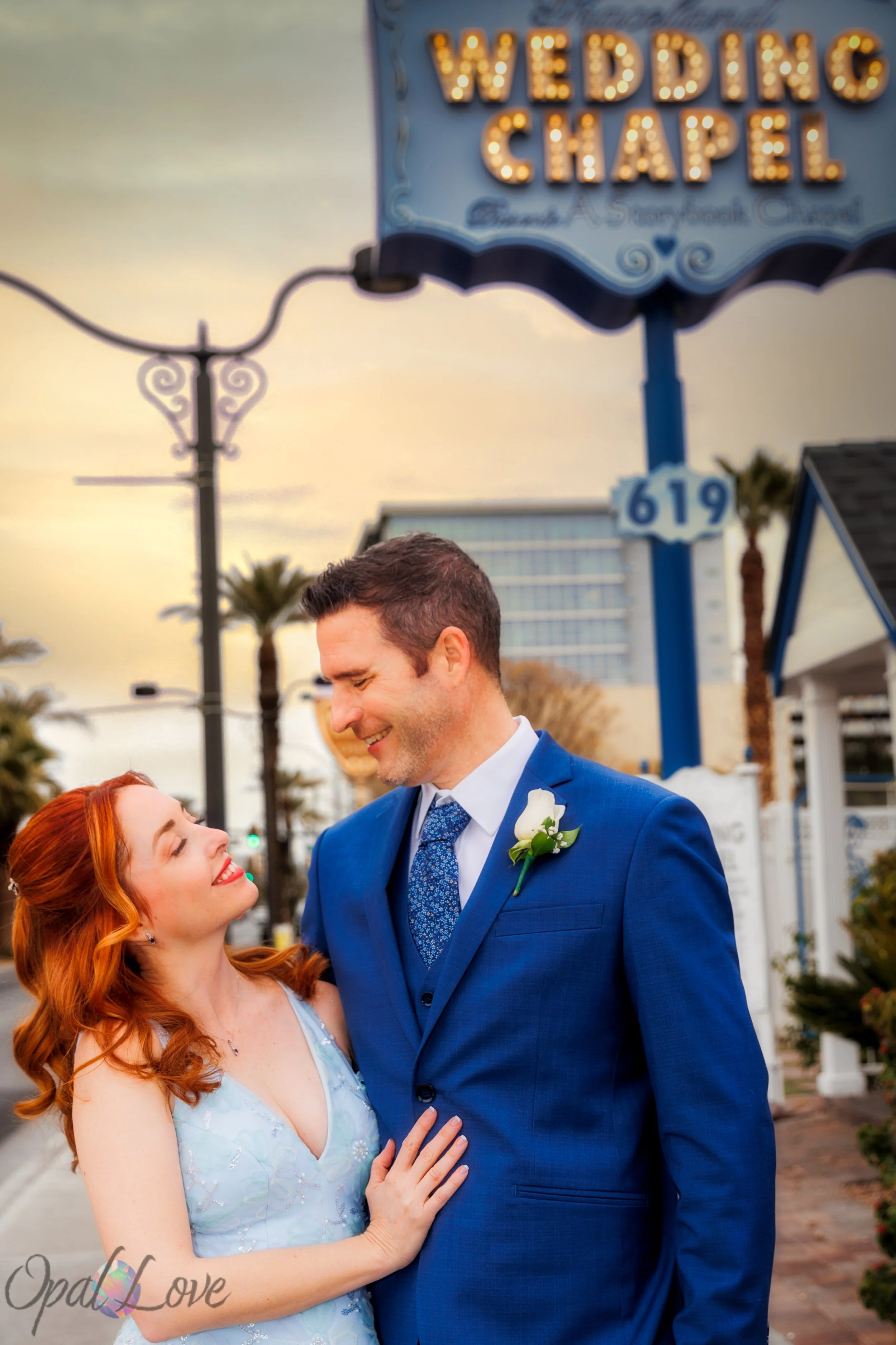 

Couple smiling at each other beneath an illuminated wedding chapel sign.