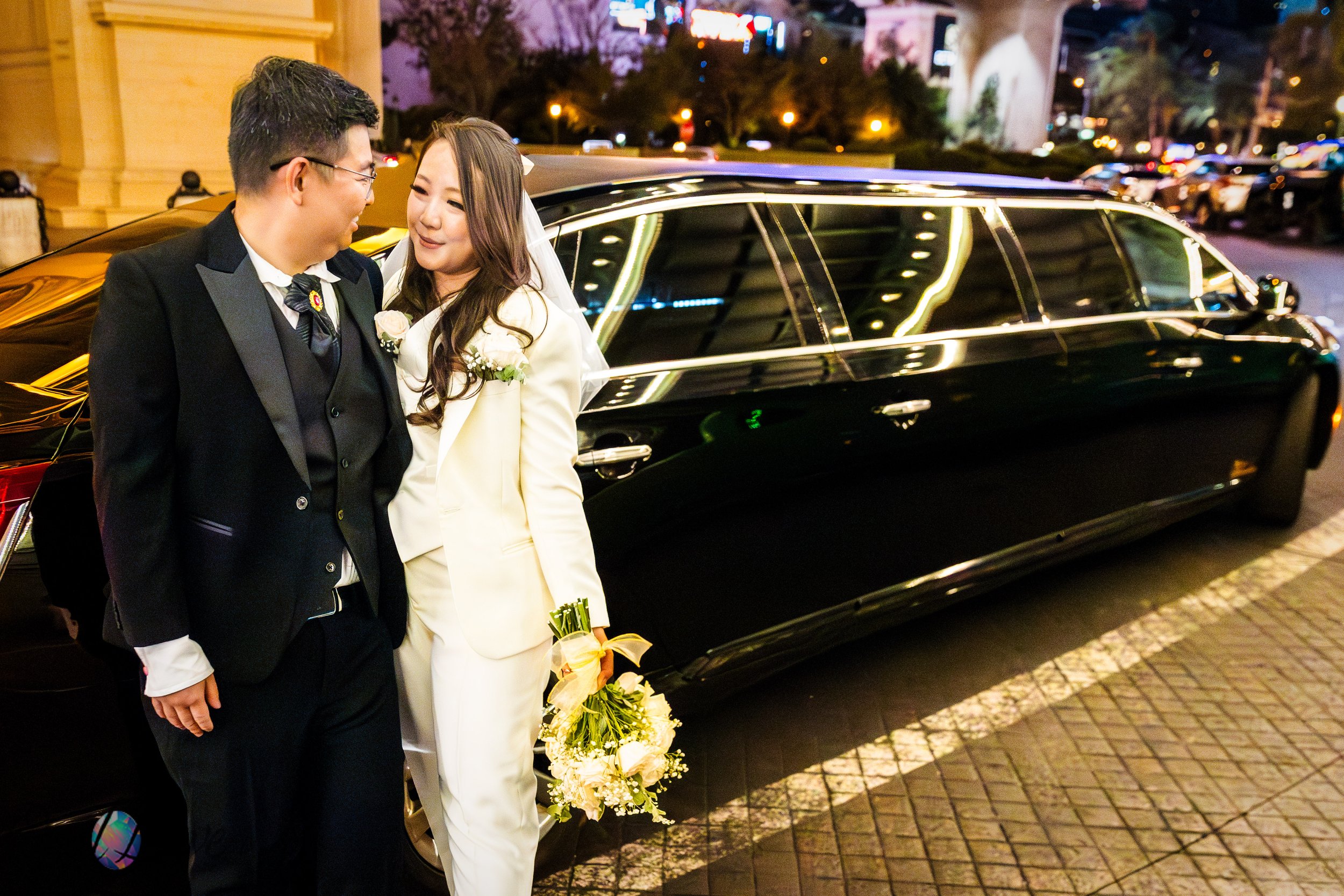 Newlyweds stand together beside a black limousine in Las Vegas