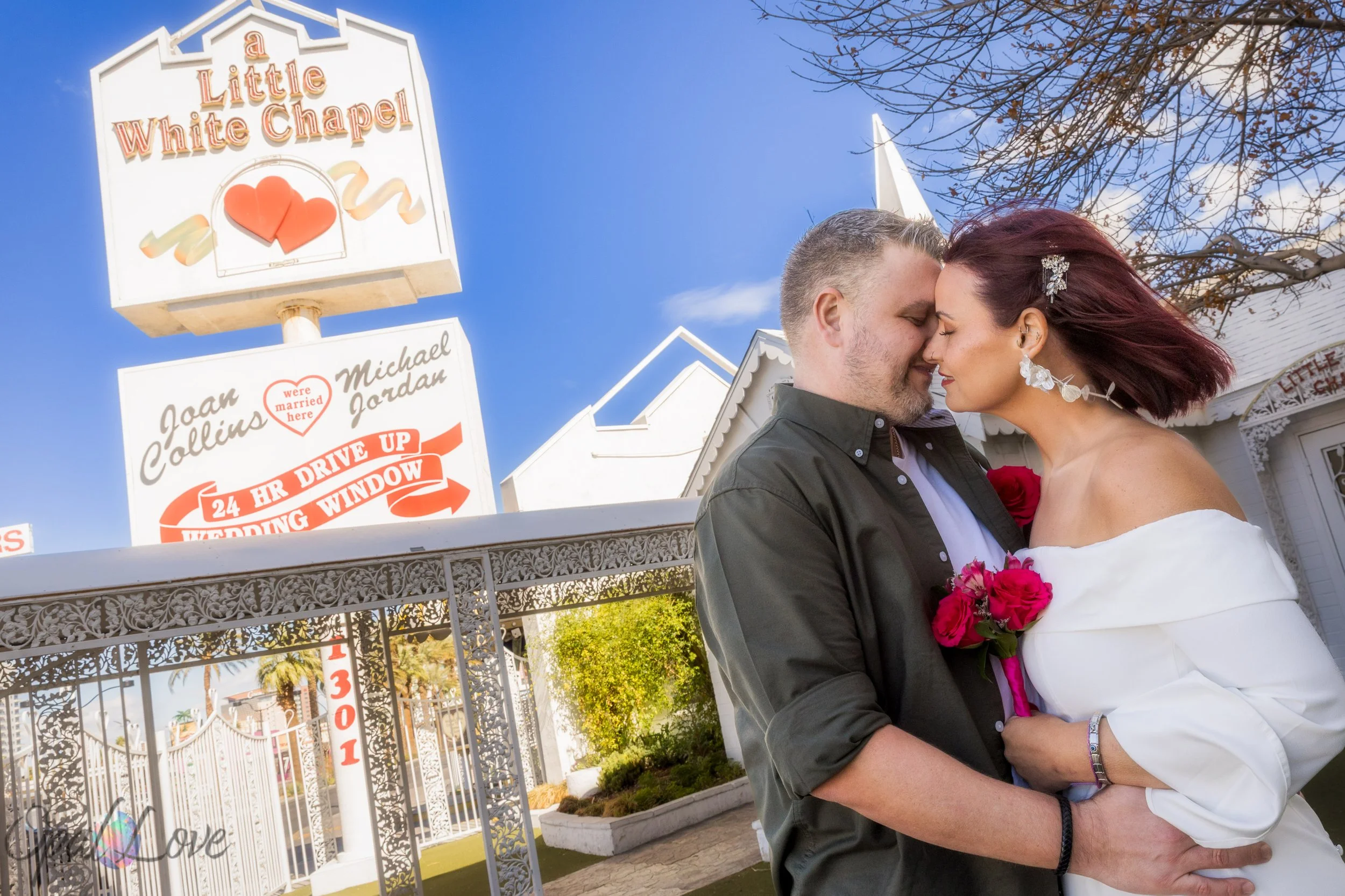 Bride and groom embracing by the Little White Chapel sign and white gates in Las Vegas.