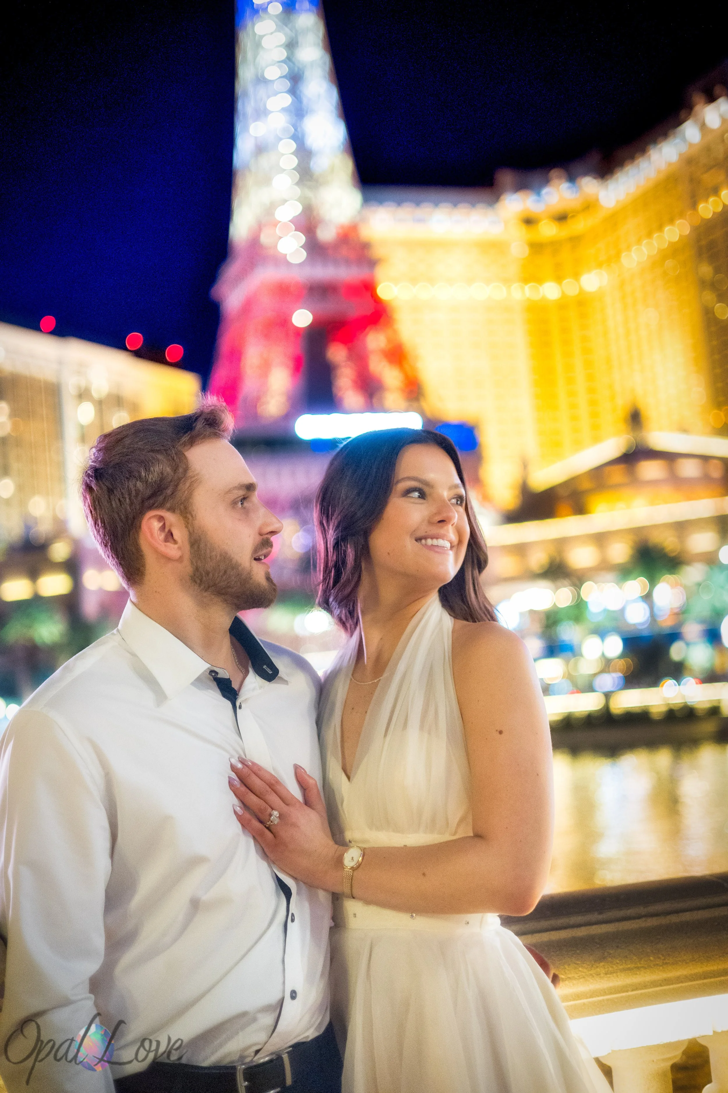 Newlyweds standing close together with Las Vegas Strip lights glowing behind them near Paris Las Vegas.