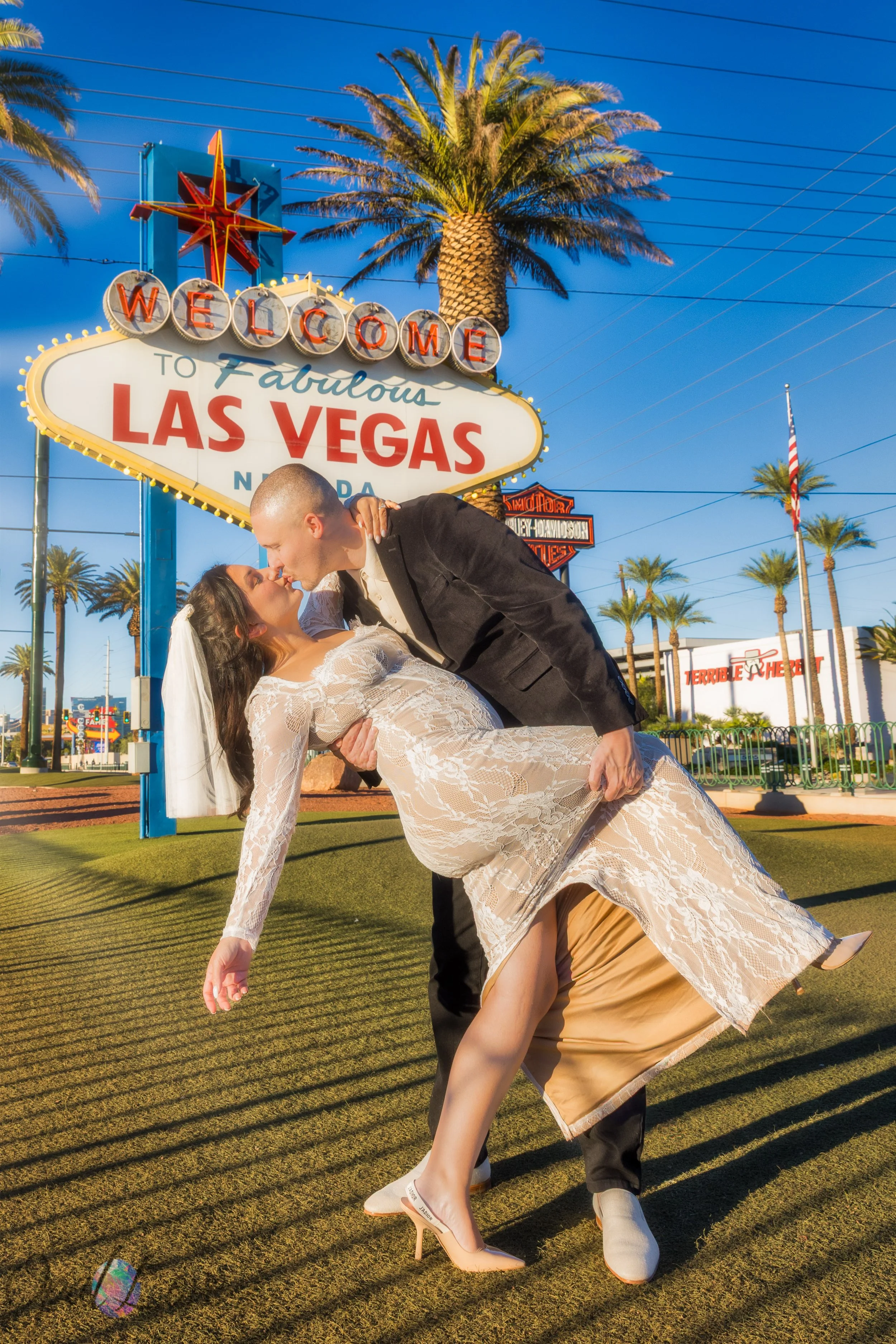 Couple sharing a dip kiss in front of the Welcome to Las Vegas Sign in bright golden sunlight.
