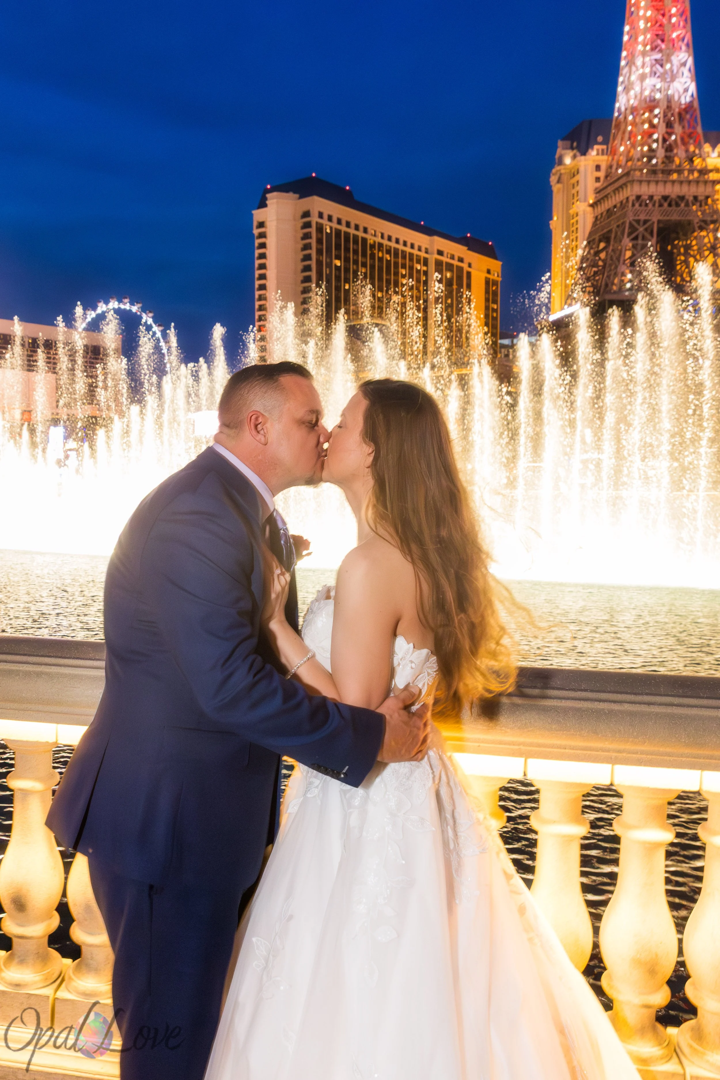 Wedding couple kissing near the Bellagio fountains with the Paris Las Vegas Eiffel Tower behind them.