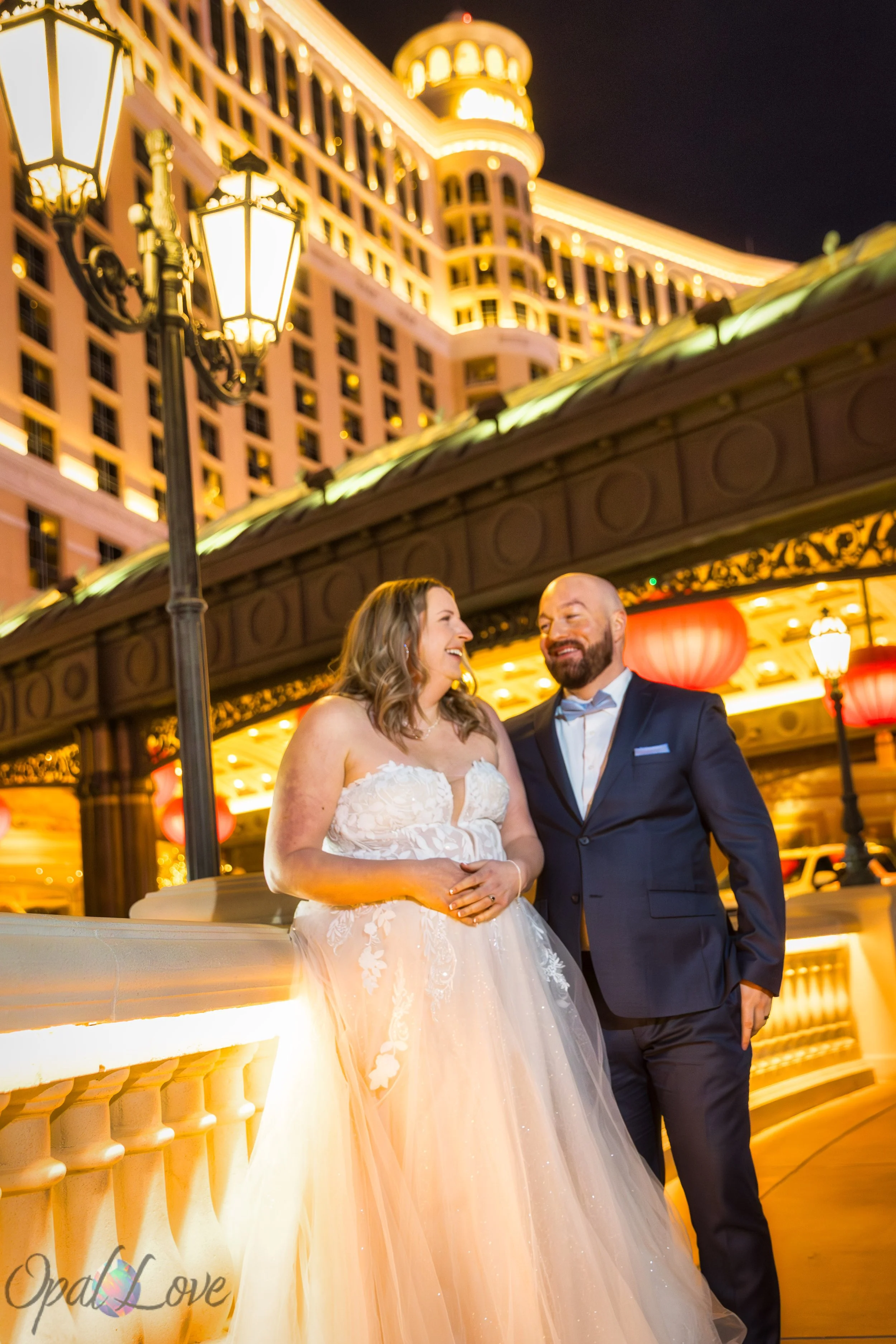 Bride and groom laughing together outside the Bellagio Hotel on the Las Vegas Strip at night.