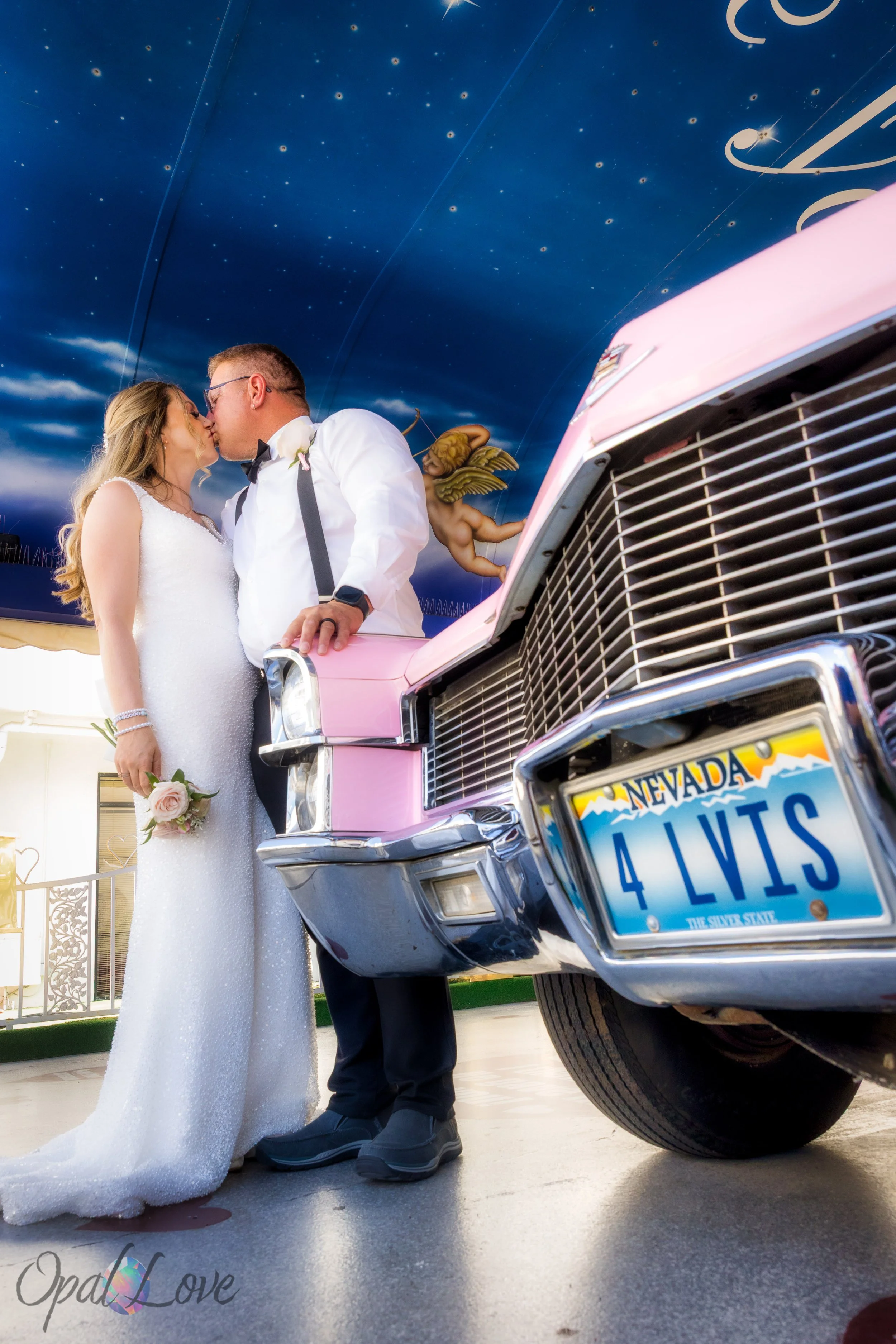 Couple sharing a kiss beside pink Cadillac with 4 LVIS license plate.