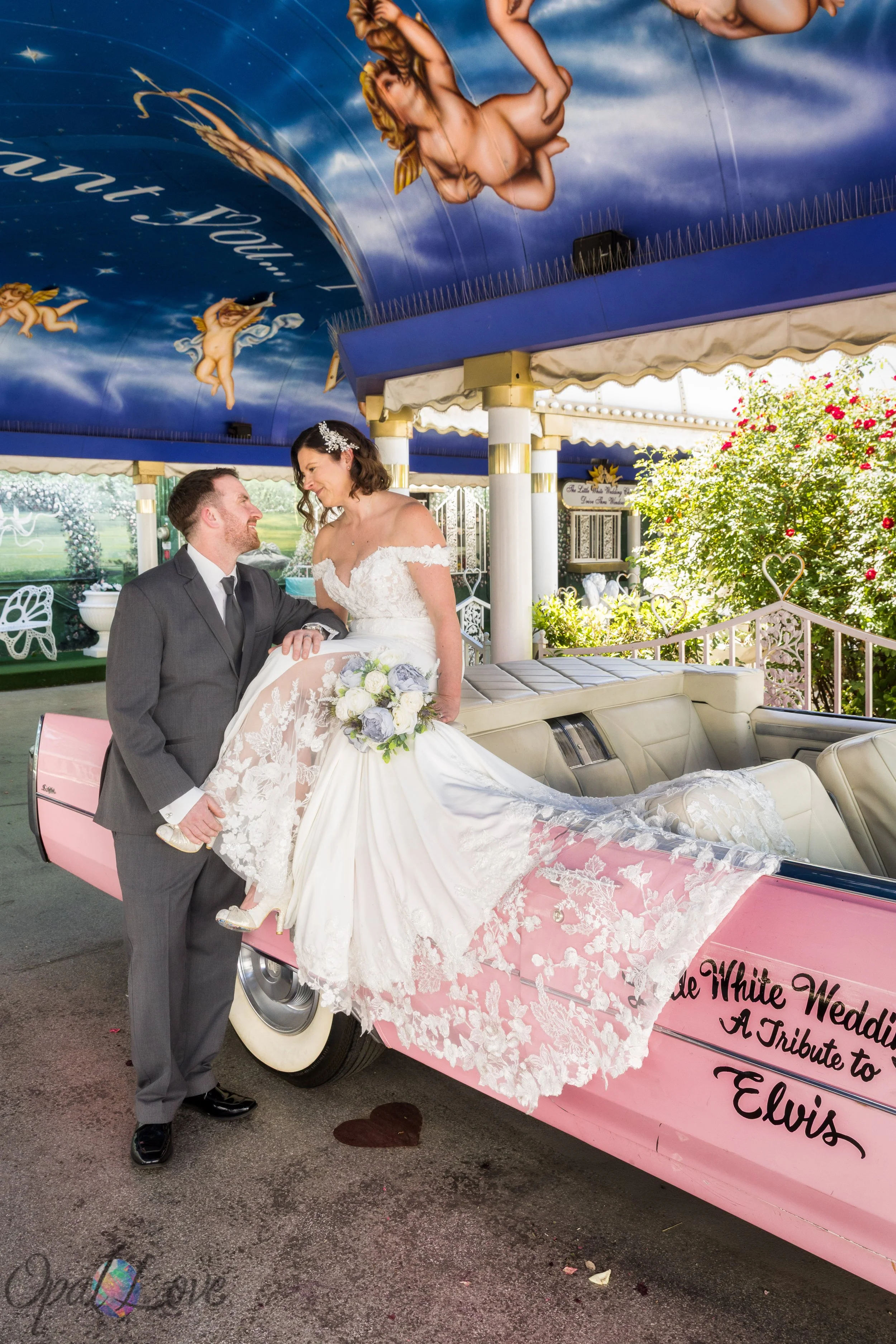 Groom lifting bride onto a pink Cadillac during their fun Las Vegas elopement photo session.